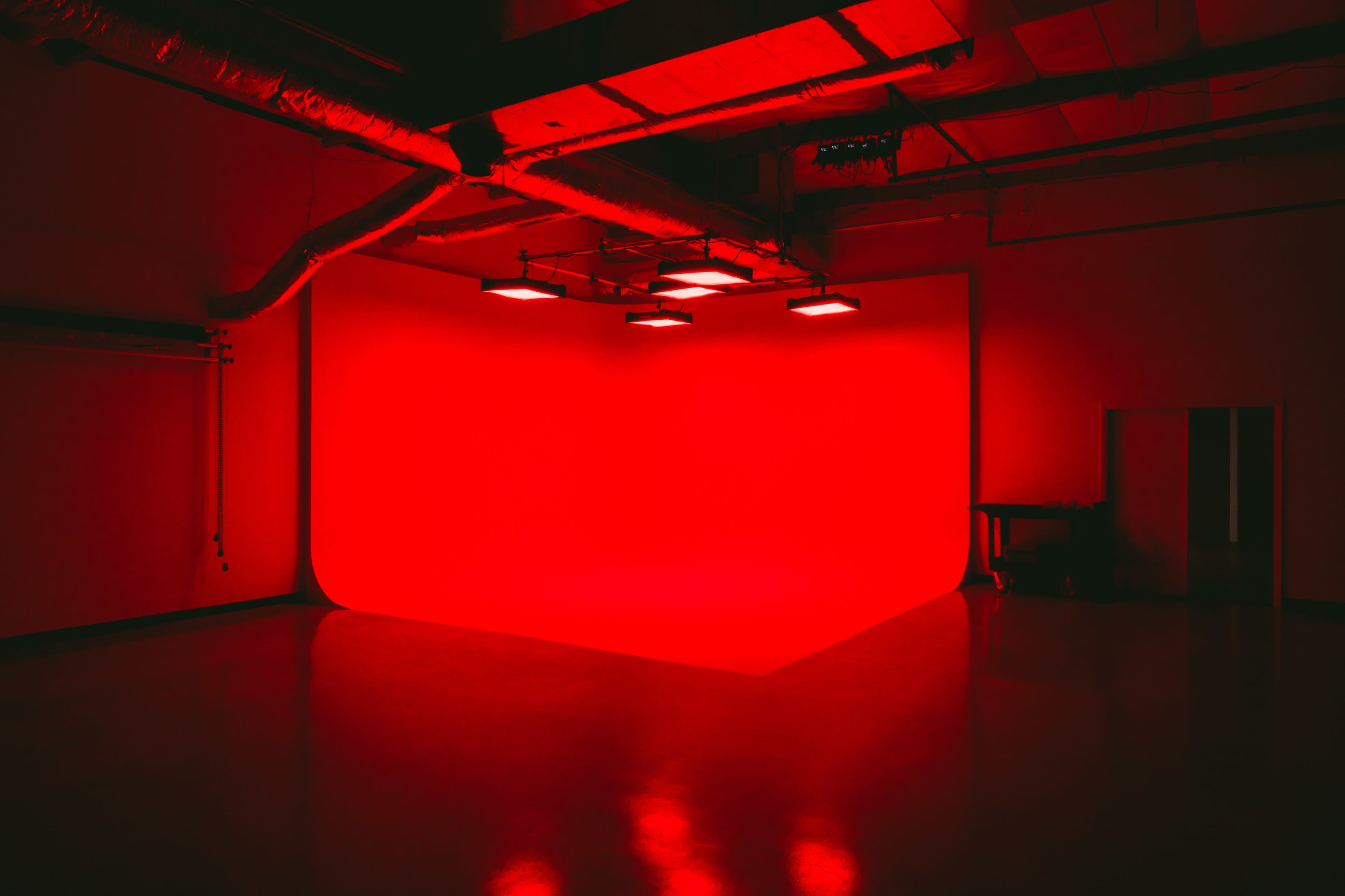 A dimly lit studio features a bright red backdrop illuminated by overhead lights.