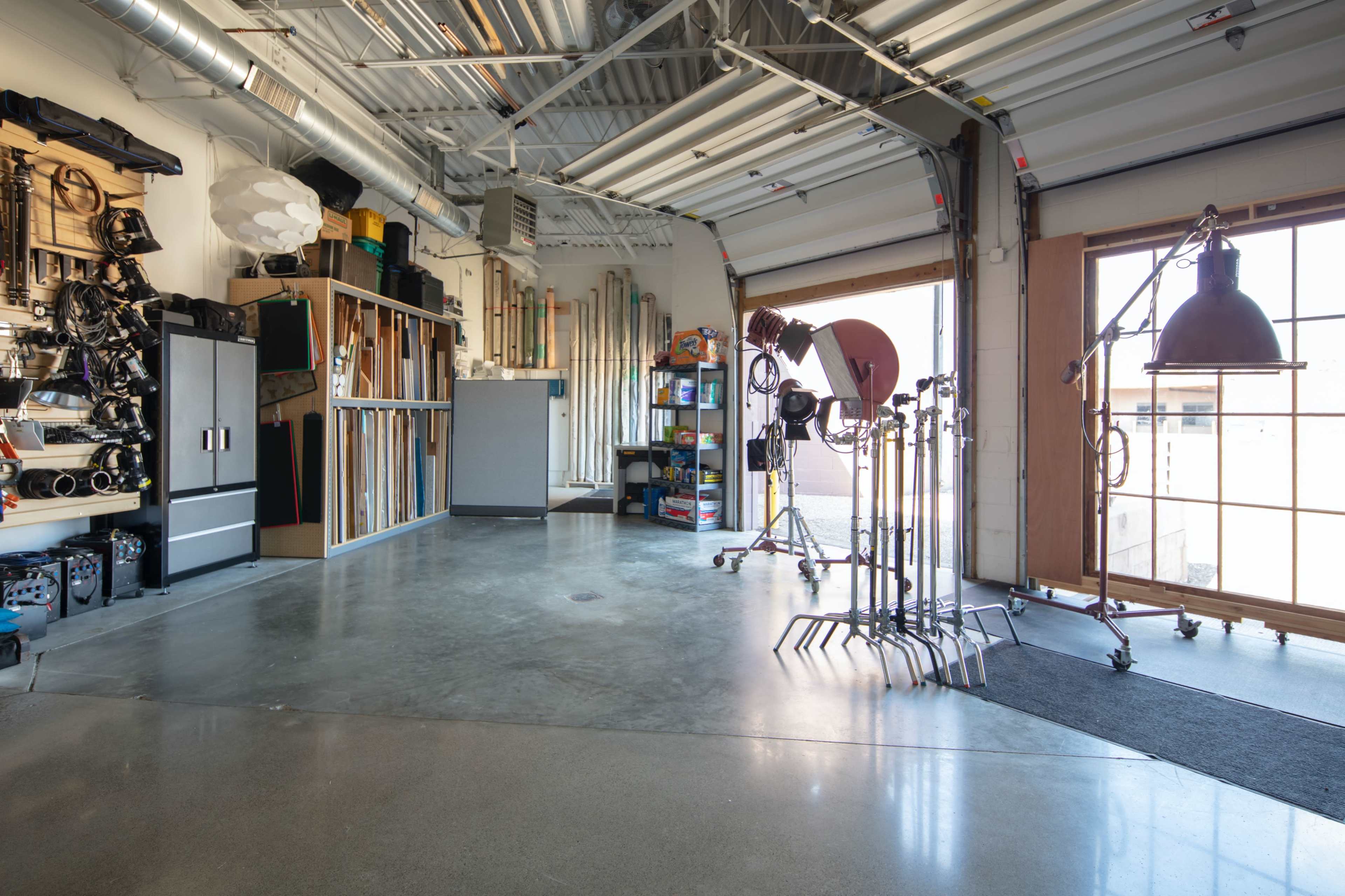 A spacious garage filled with various tools, equipment, and lighting stands arranged along the walls and center.