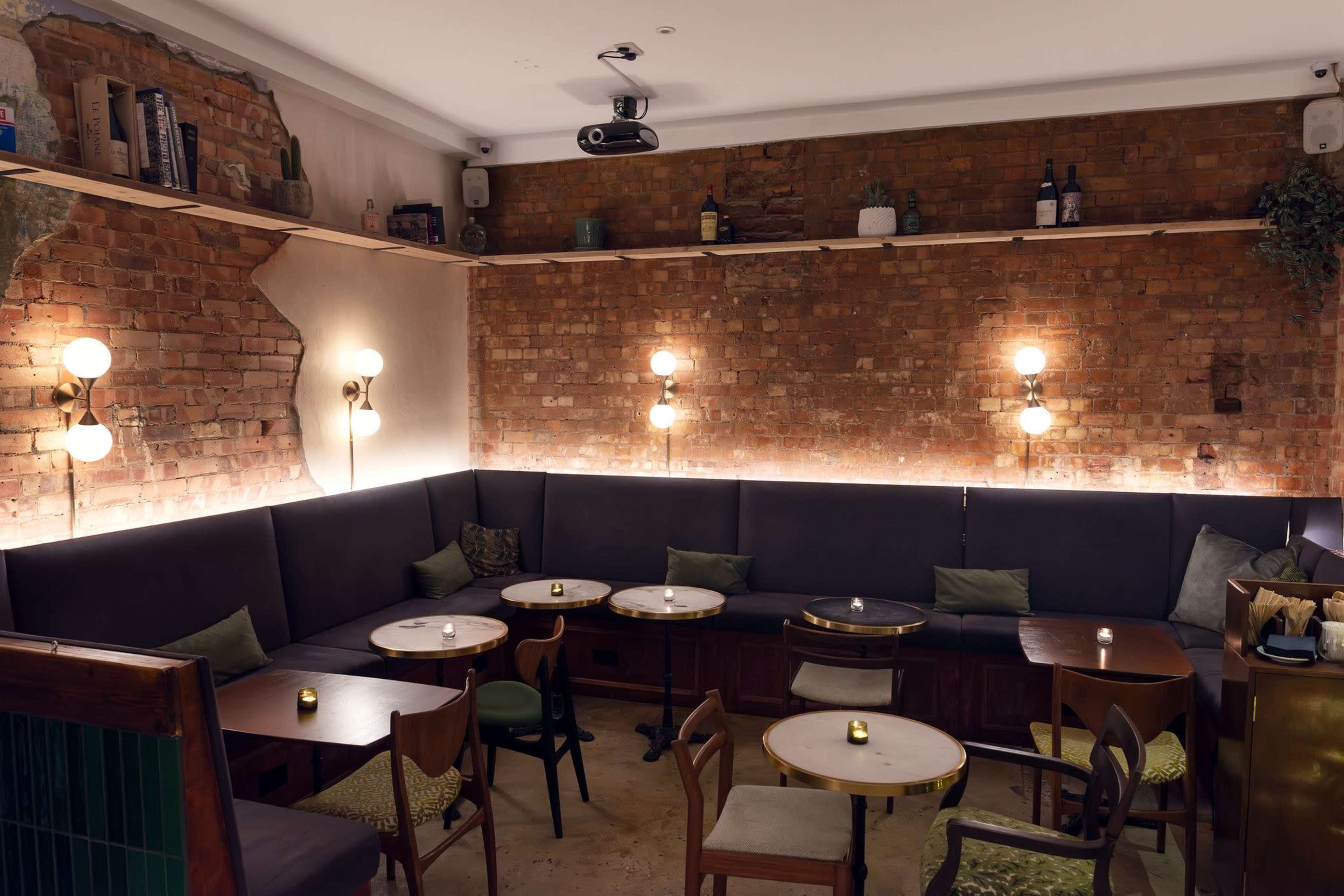 The image showcases a cozy café interior featuring exposed brick walls, intimate seating areas with dark upholstery, and warm lighting fixtures.