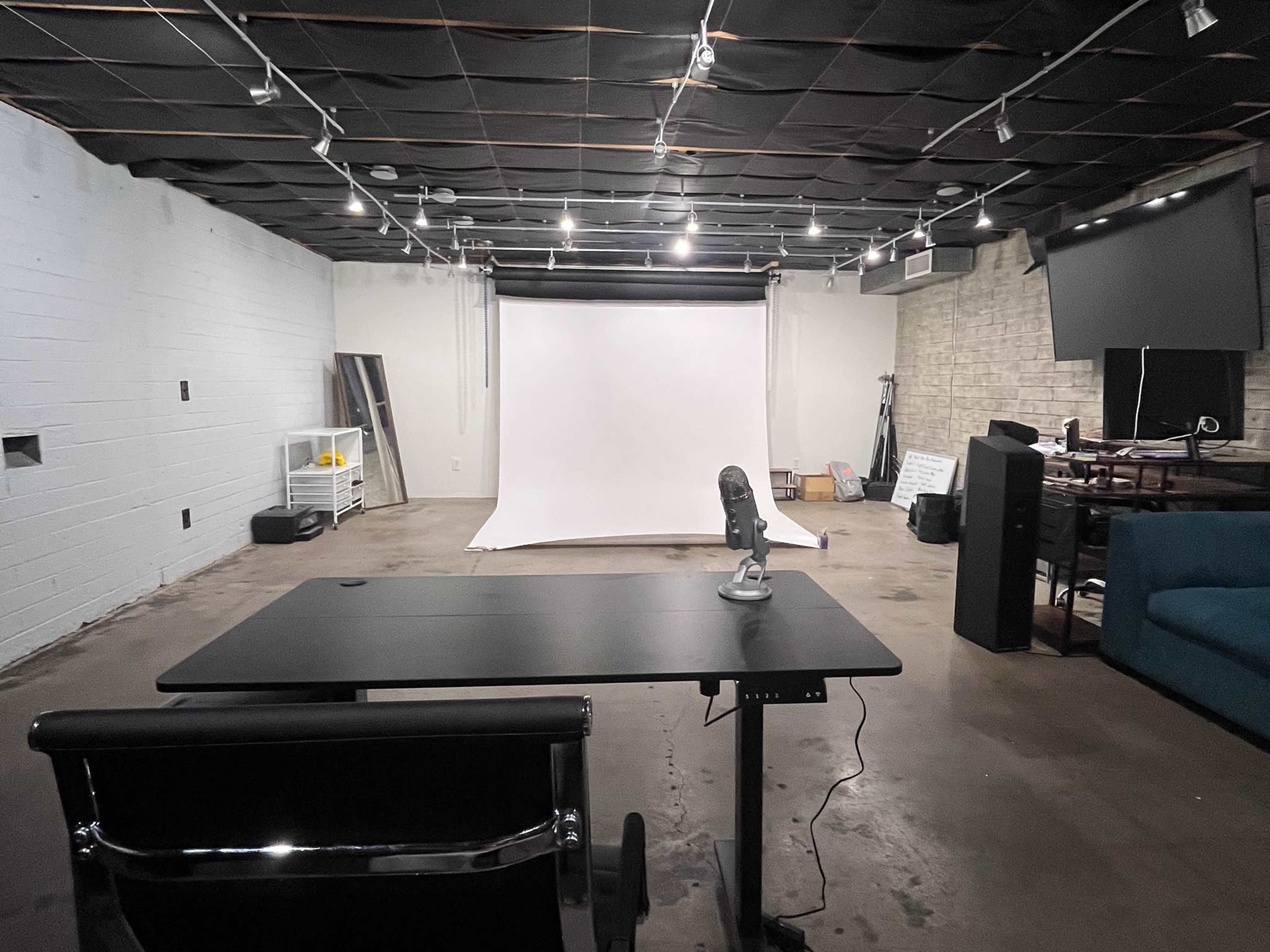 A spacious, well-lit studio with a white backdrop, a desk and chair, and various equipment arranged around the room.