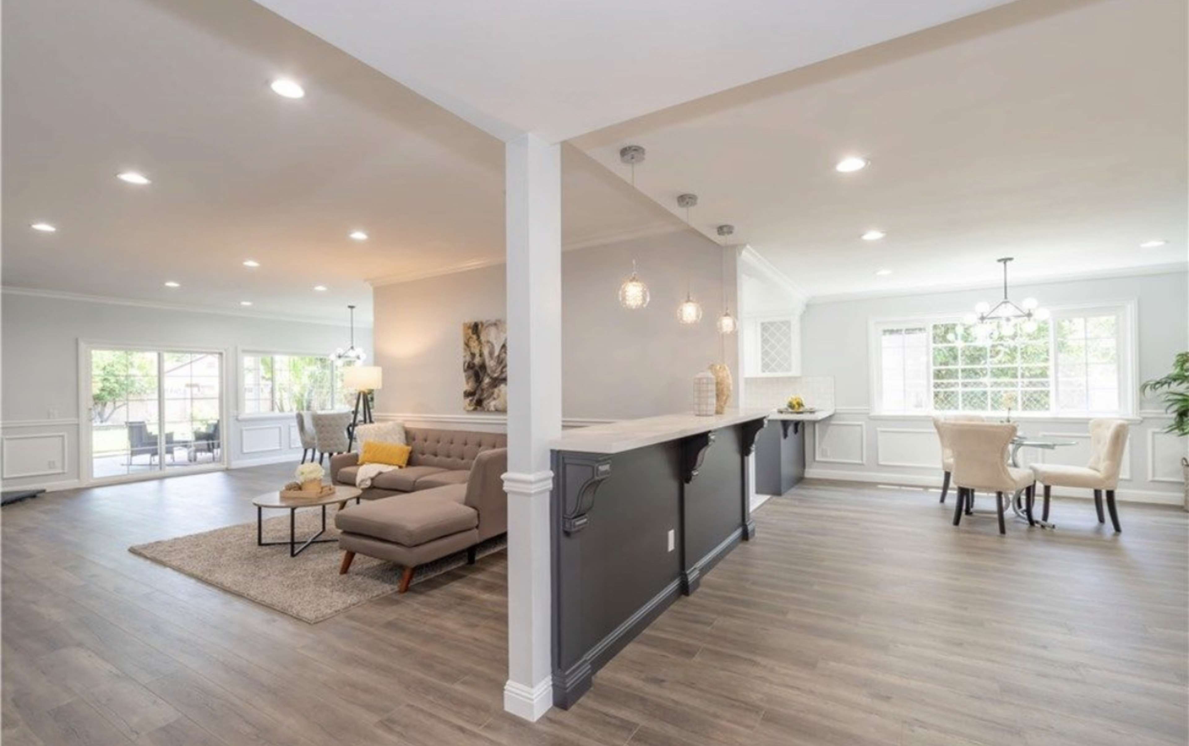 A modern open-concept living space featuring a beige sofa, a coffee table, and a dining area with two chairs, illuminated by pendant lighting.