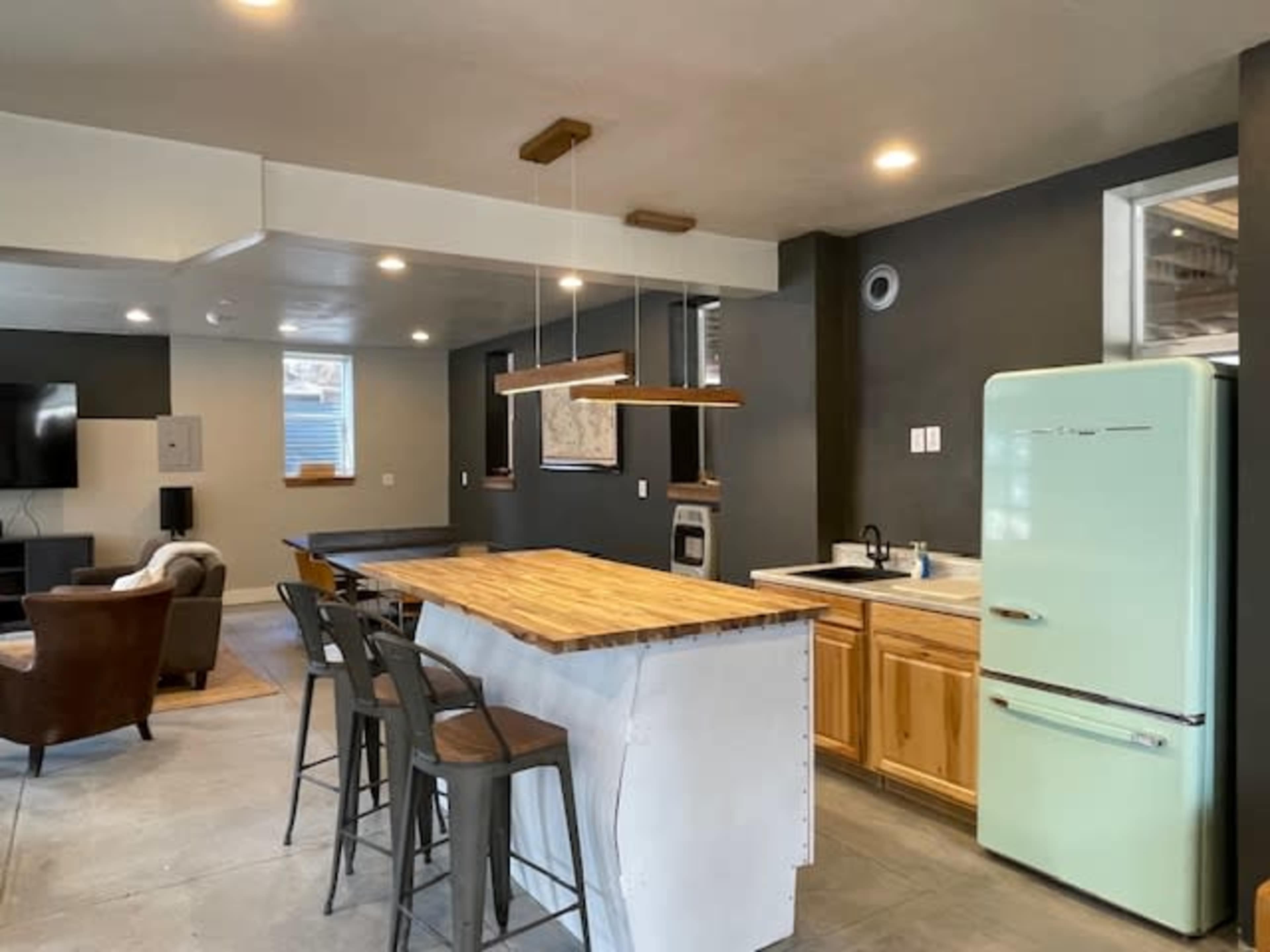 A modern kitchen with a wooden island, gray walls, and a retro mint green refrigerator.