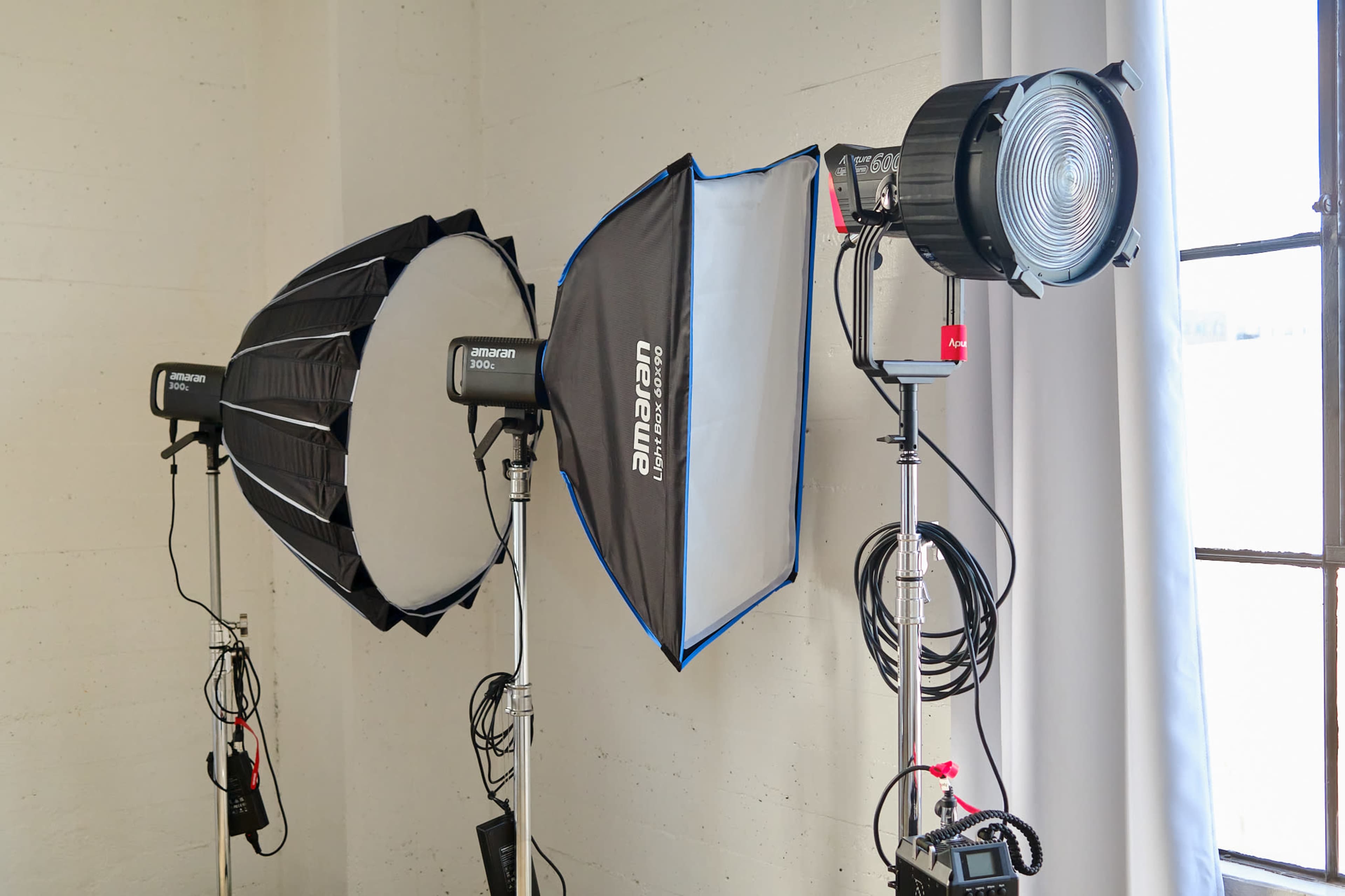 The image shows three professional studio lighting setups, including softboxes and a spotlight, arranged against a light-colored wall.