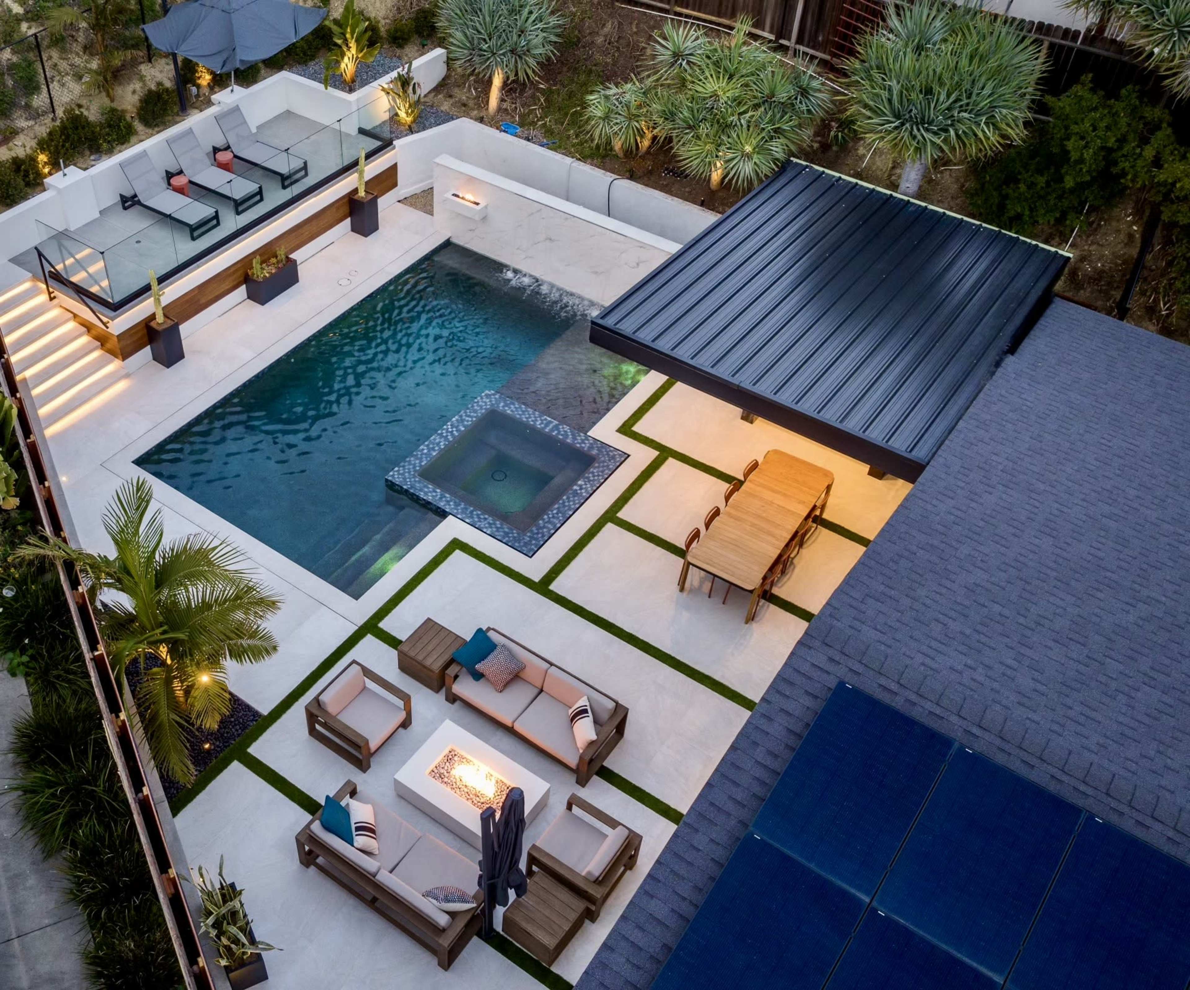 The image shows a modern outdoor pool area featuring a swimming pool, hot tub, lounge chairs, a dining table, and landscaped greenery.