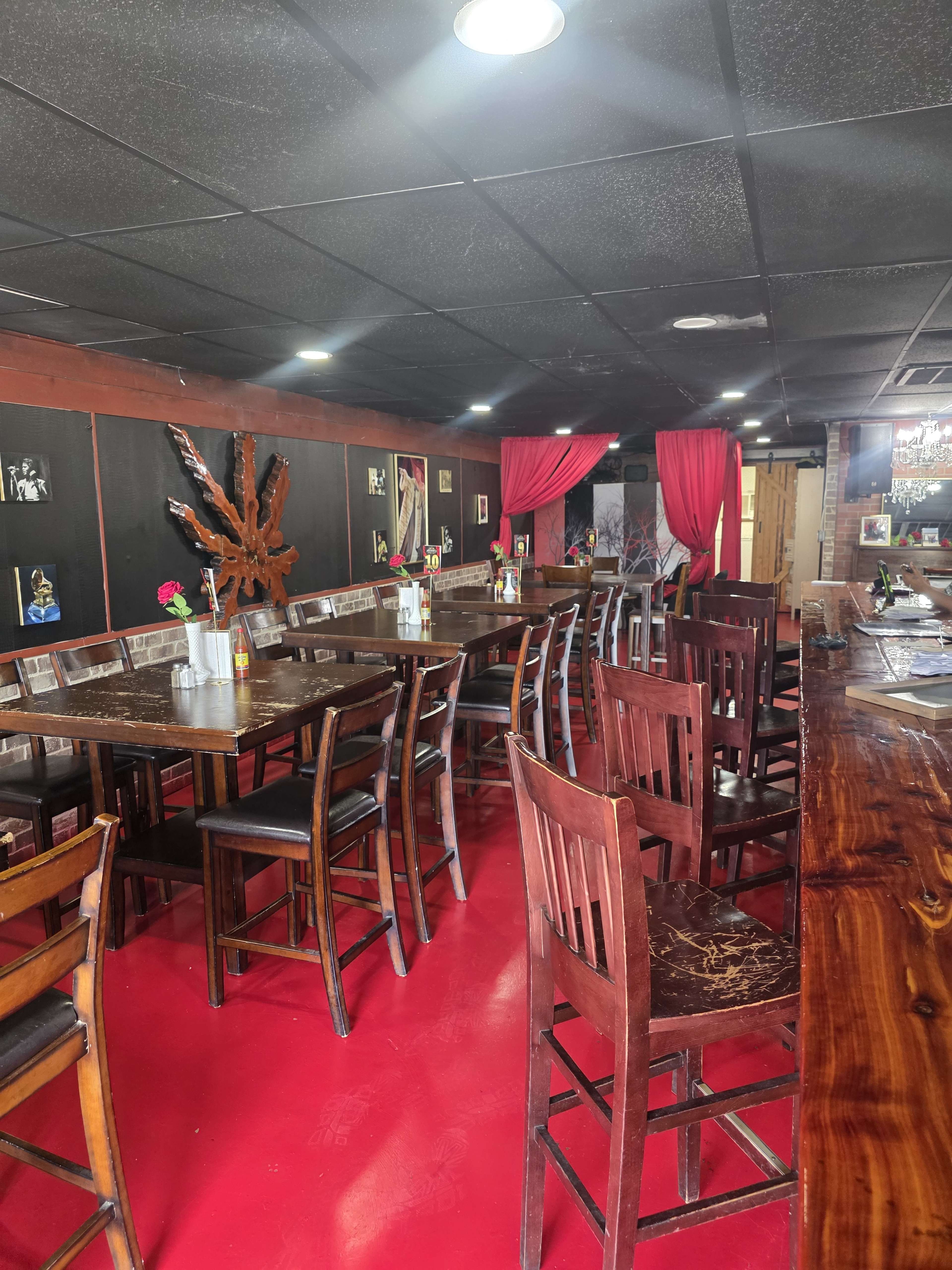 The image shows the interior of a restaurant featuring wooden tables and chairs, red flooring, and decorative black walls with framed photos.