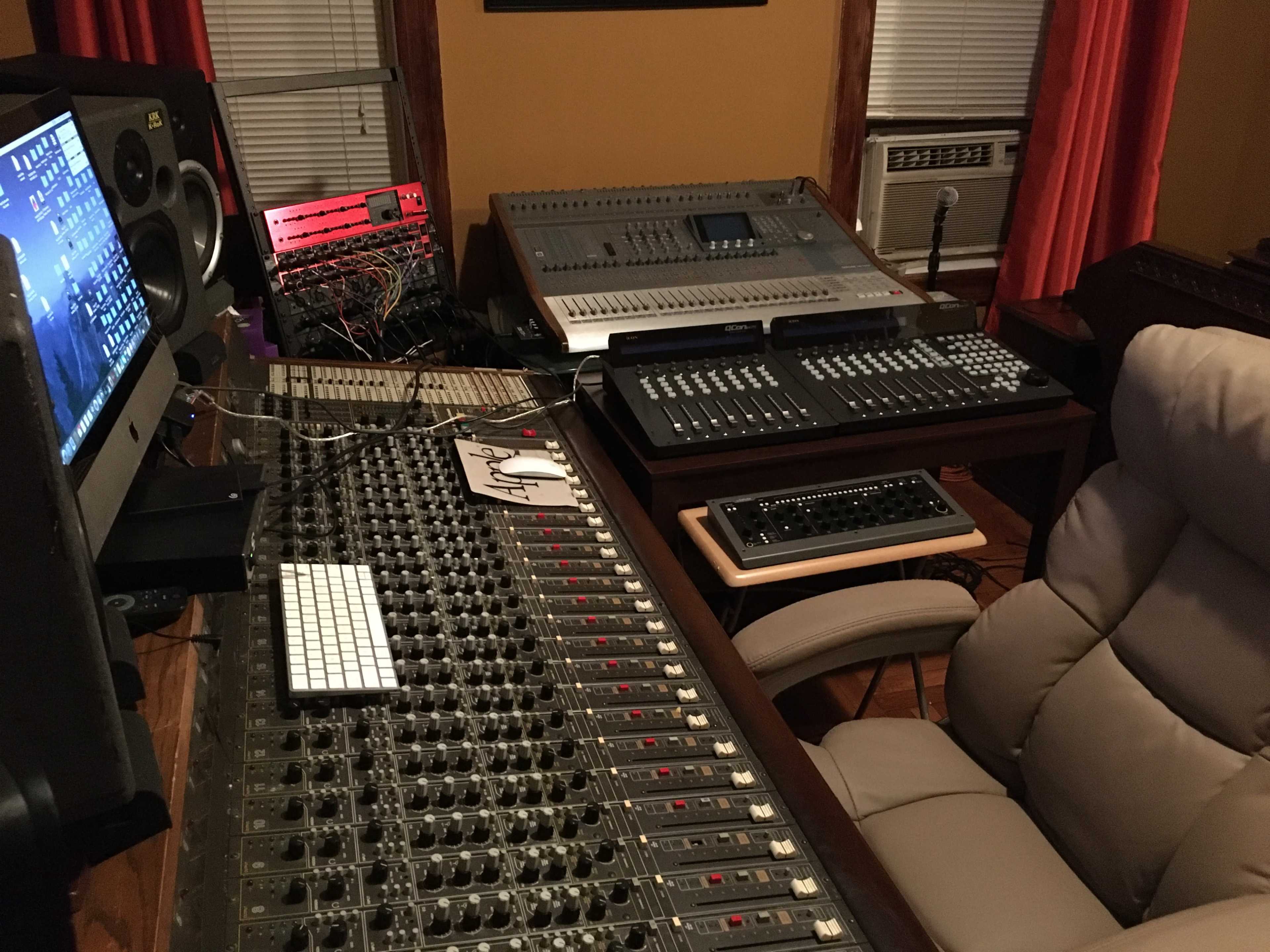 A recording studio with a sound mixing console, a computer monitor, and various audio equipment arranged around a comfortable chair.