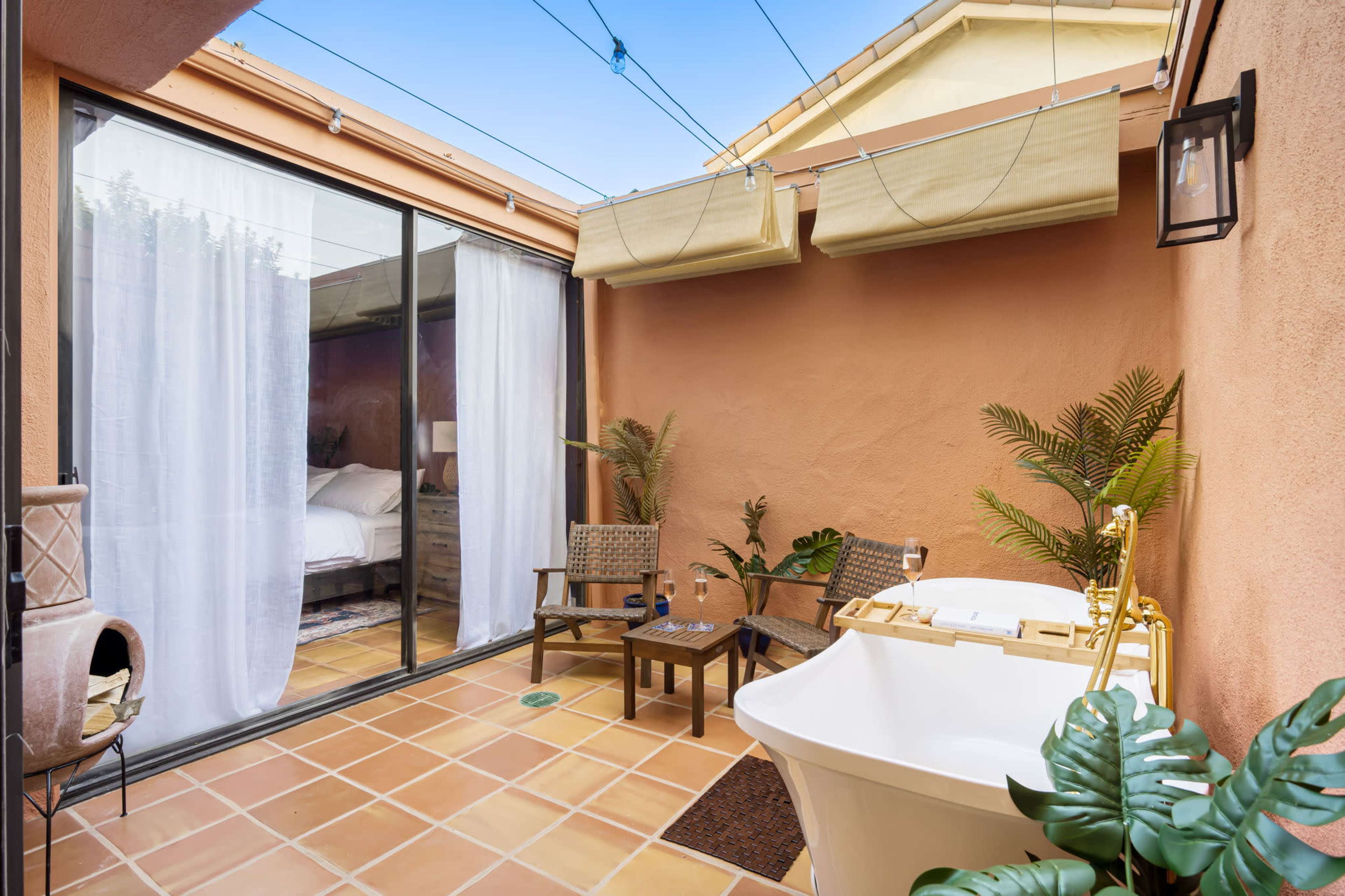 A private courtyard features a freestanding bathtub, two chairs, and sliding glass doors leading to a bedroom.