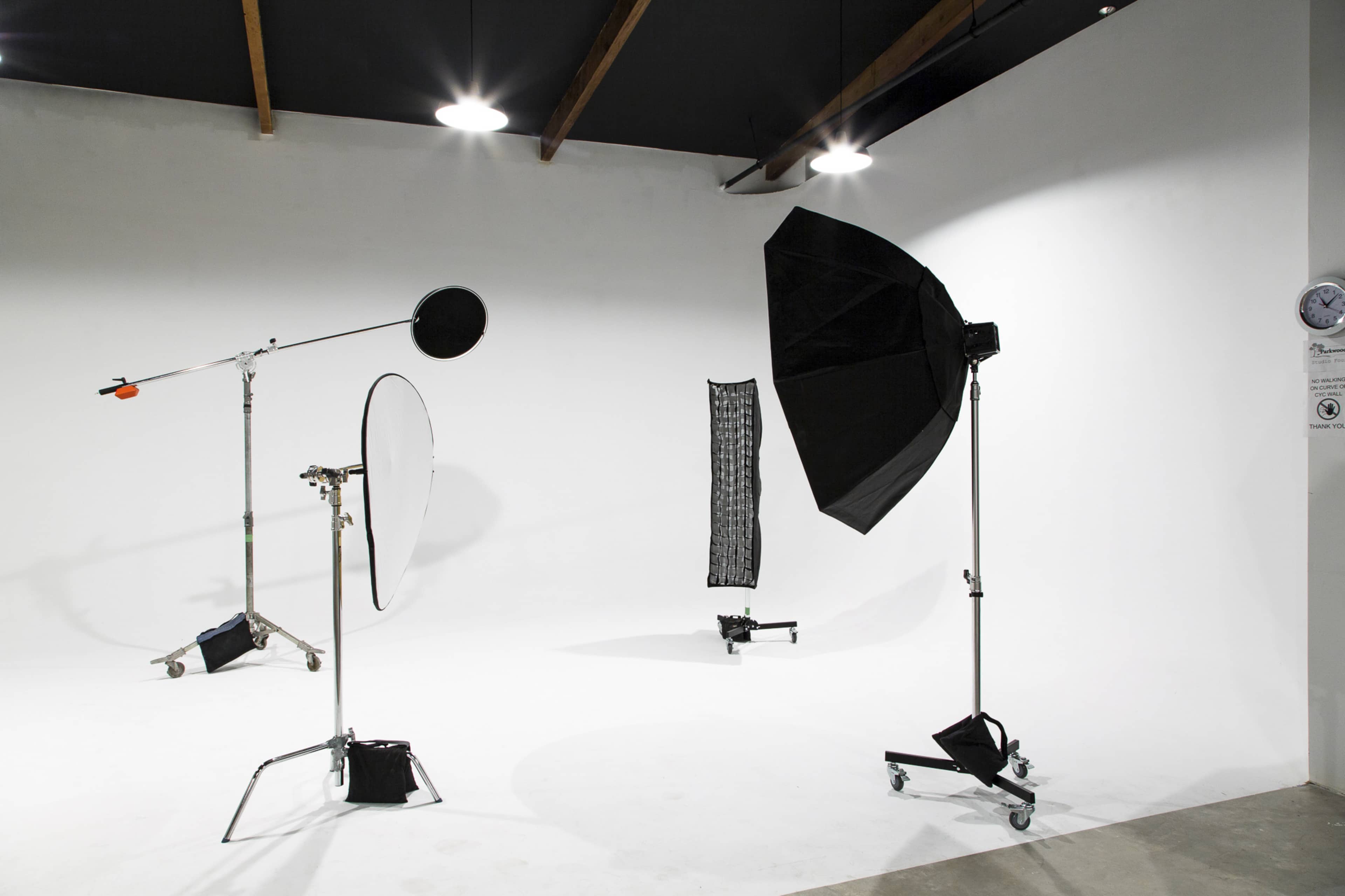 A photography studio setup with various lighting equipment, including softboxes, reflectors, and light stands against a white backdrop.