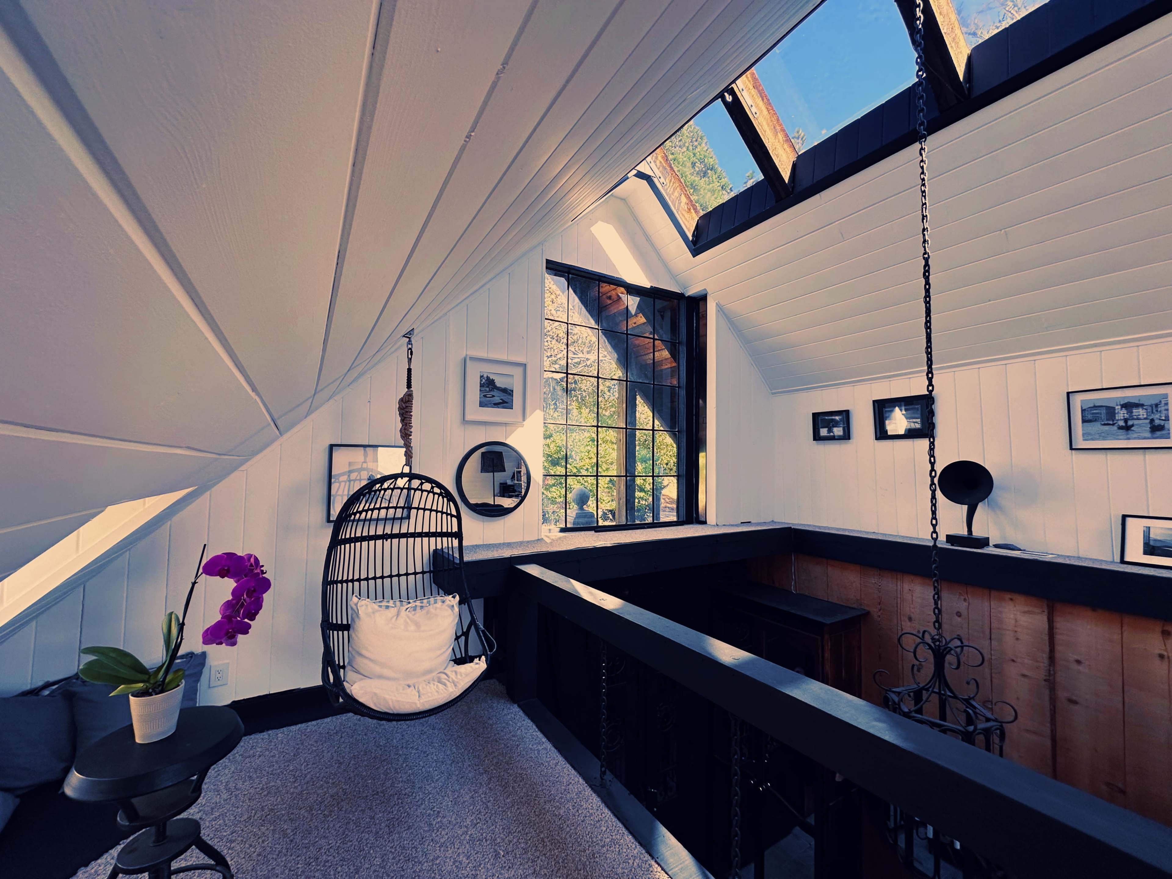 A cozy loft area with a hanging chair, large windows, and framed photographs on the walls.