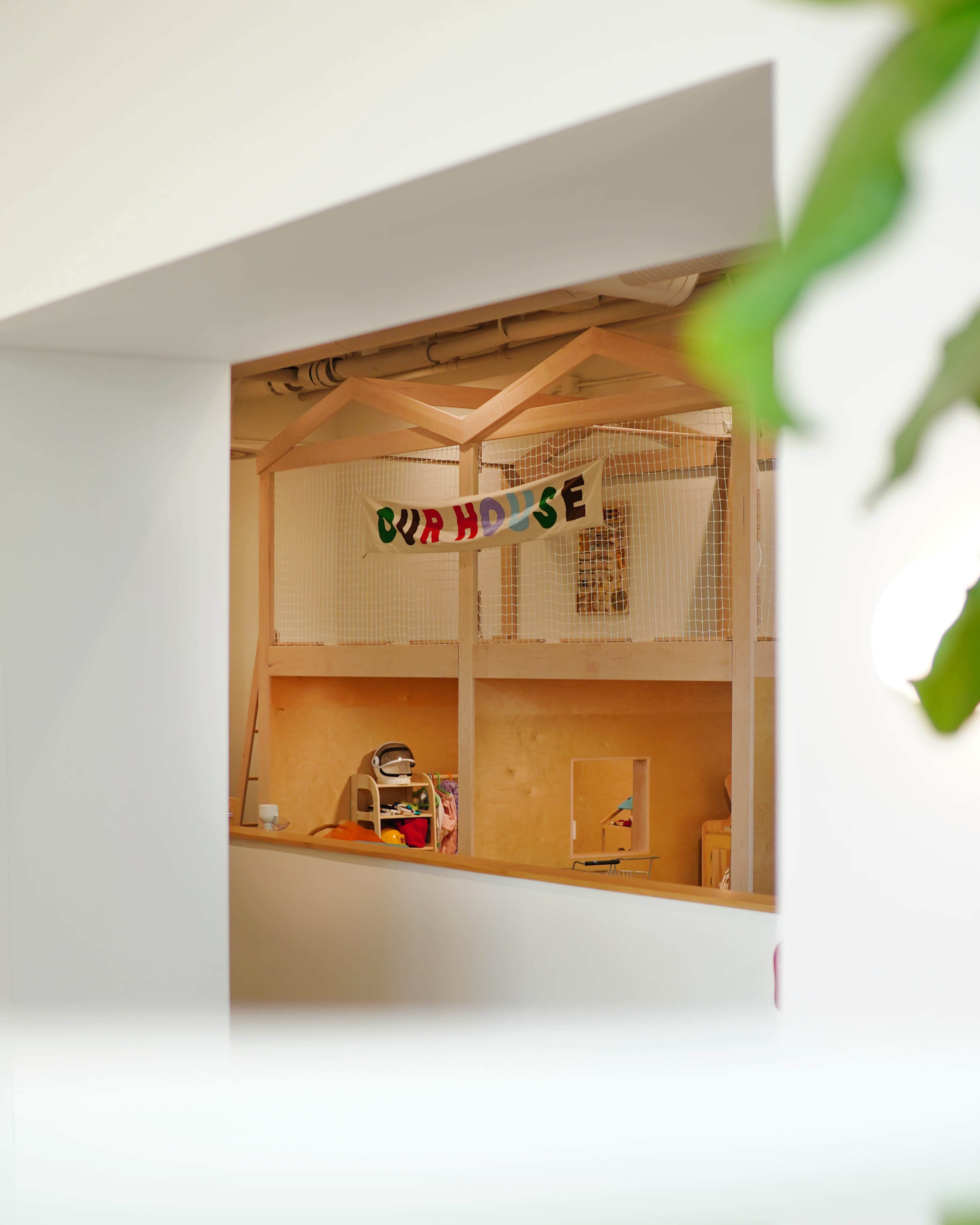 The image shows a play area enclosed by a wooden structure, featuring a colorful banner that reads "OUR HOUSE."