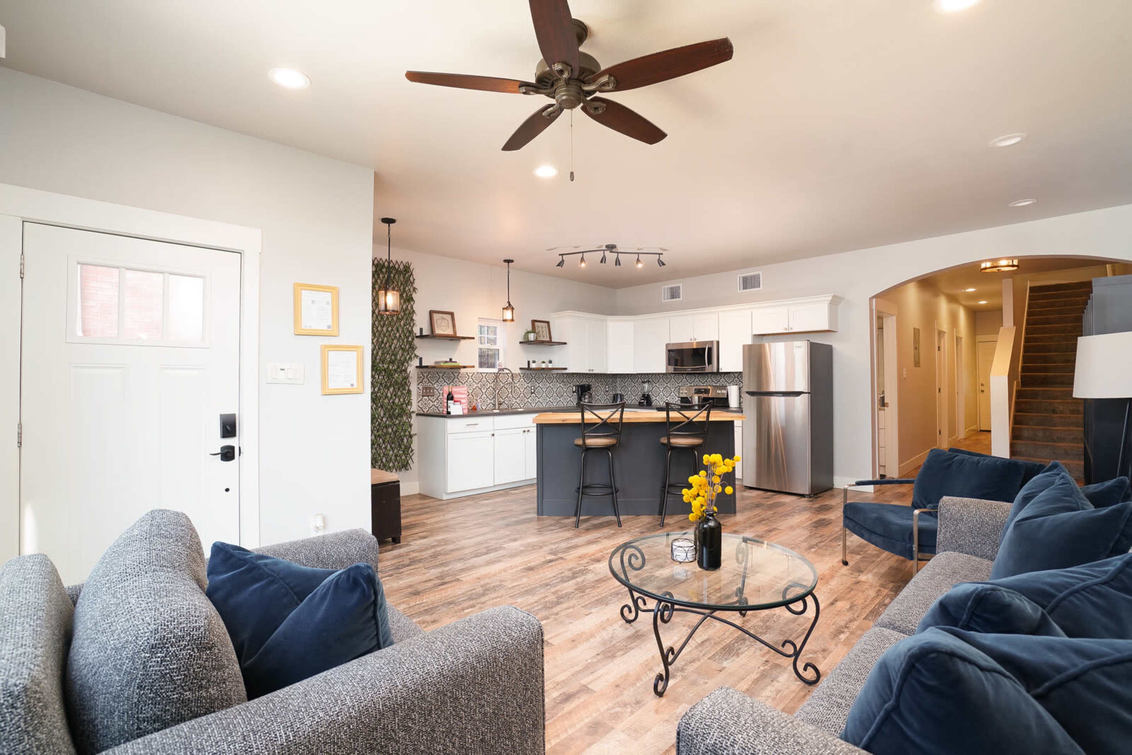 A modern living area with a kitchen bar, featuring a coffee table with flowers and a seating arrangement with gray couches.