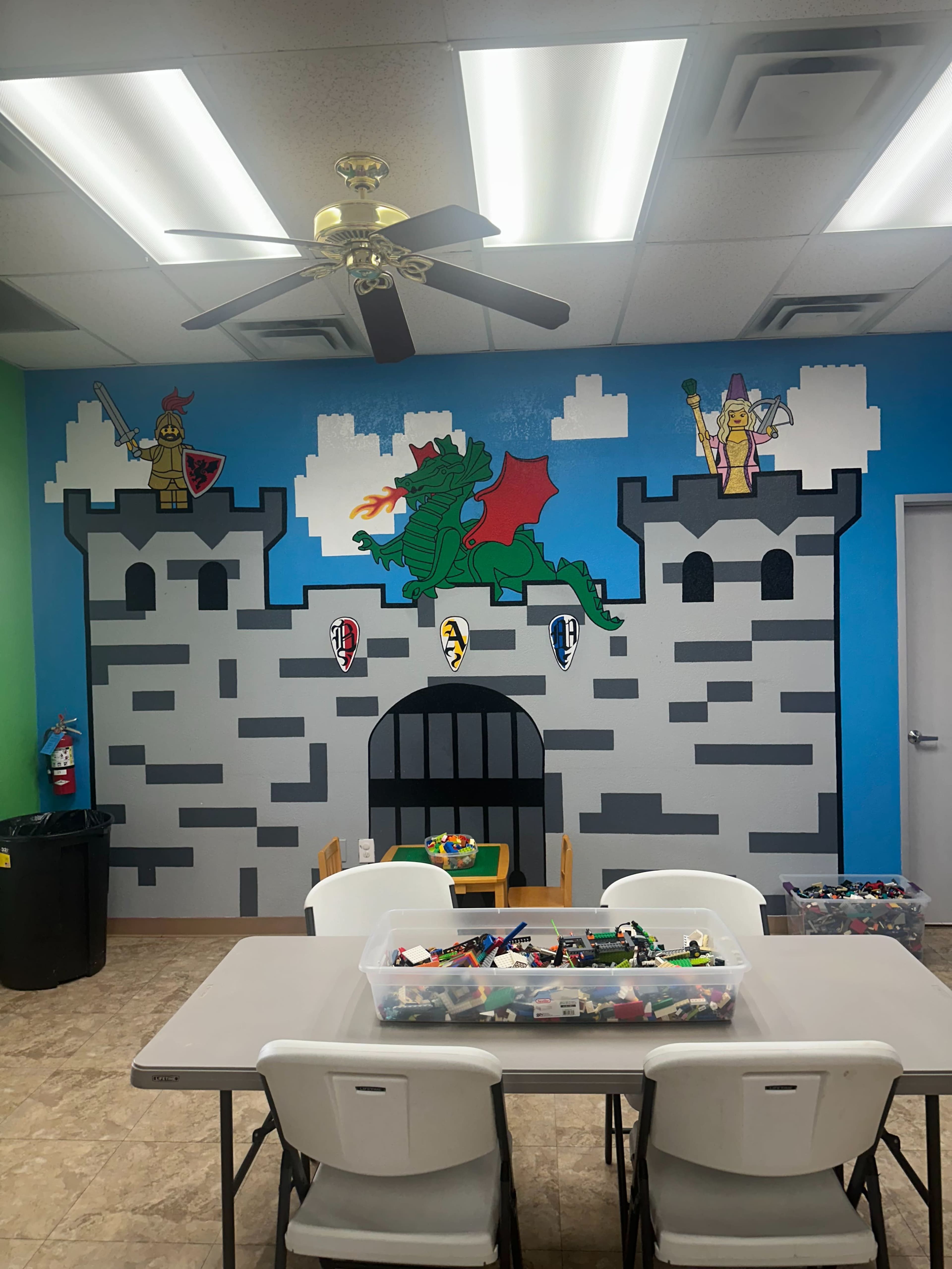 The image shows a brightly painted classroom with a castle mural on one wall and tables with containers of building blocks in the center.