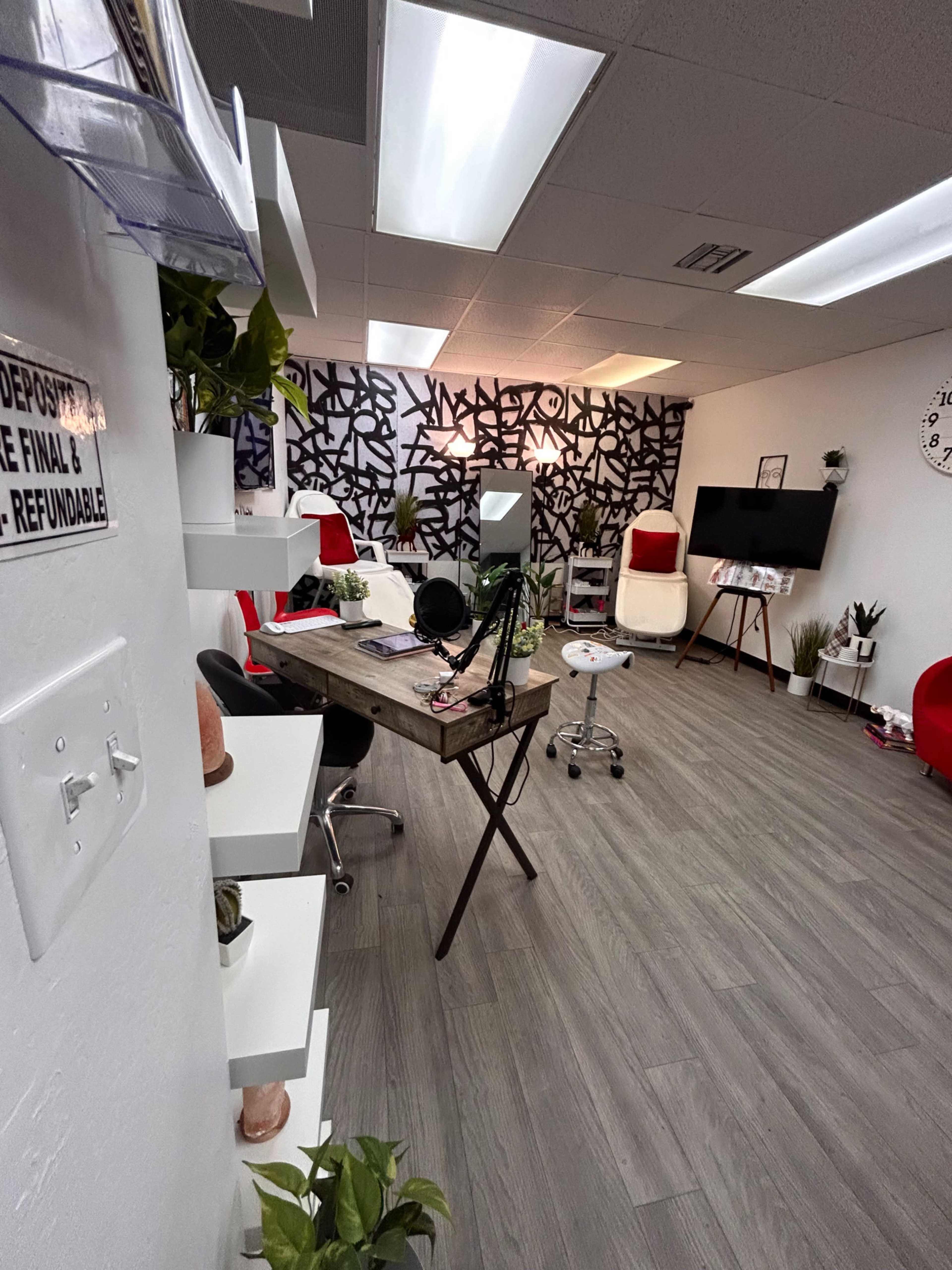 A modern office space featuring a wooden desk, white shelves, red chairs, and a patterned wall, with a microphone and a television mounted on a wall.
