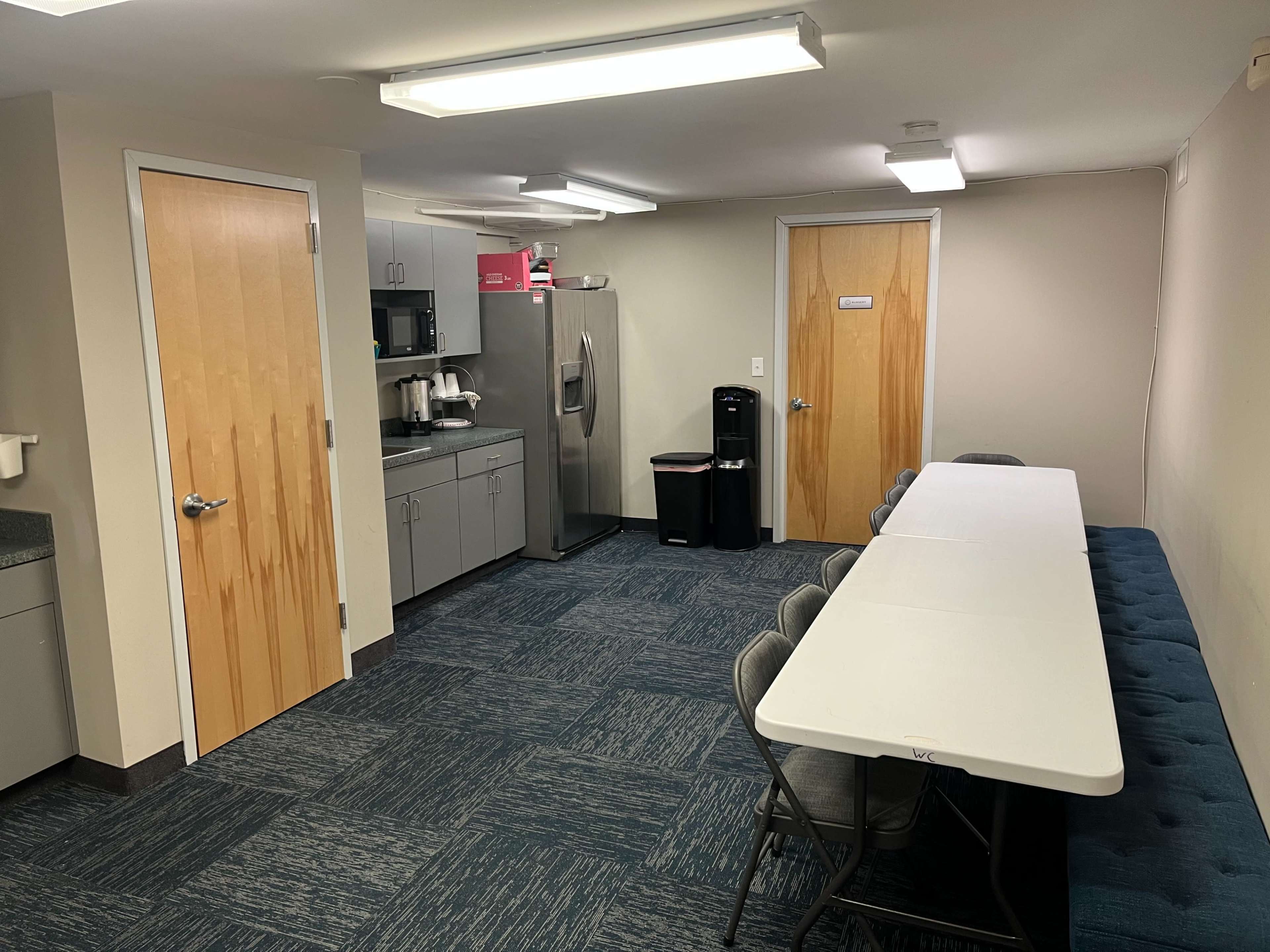 A break room features a long table with chairs, a kitchenette with appliances, and two doors leading to other areas.