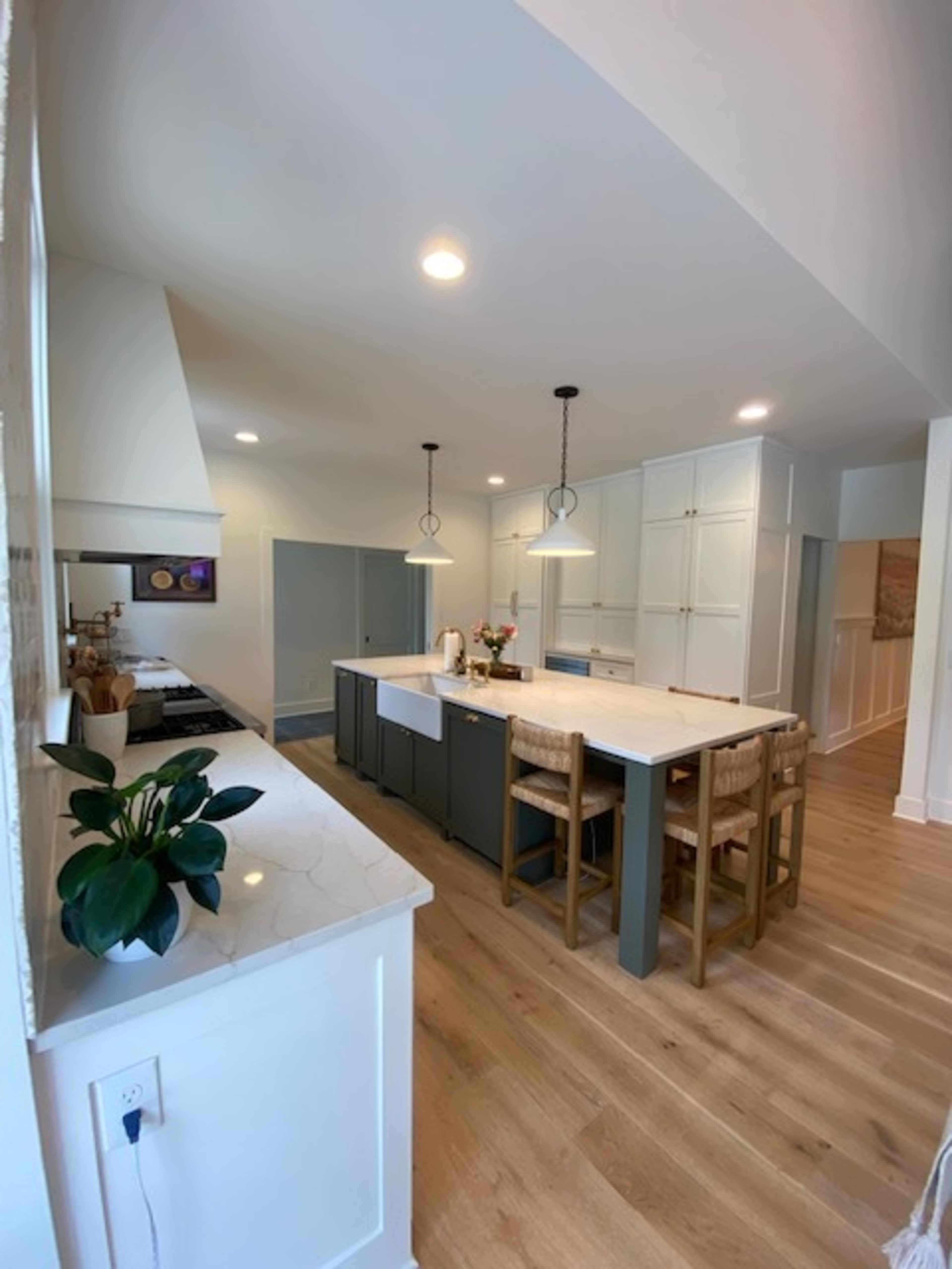 A modern kitchen with a central island, bar seating, and light-colored cabinetry set against wooden flooring.