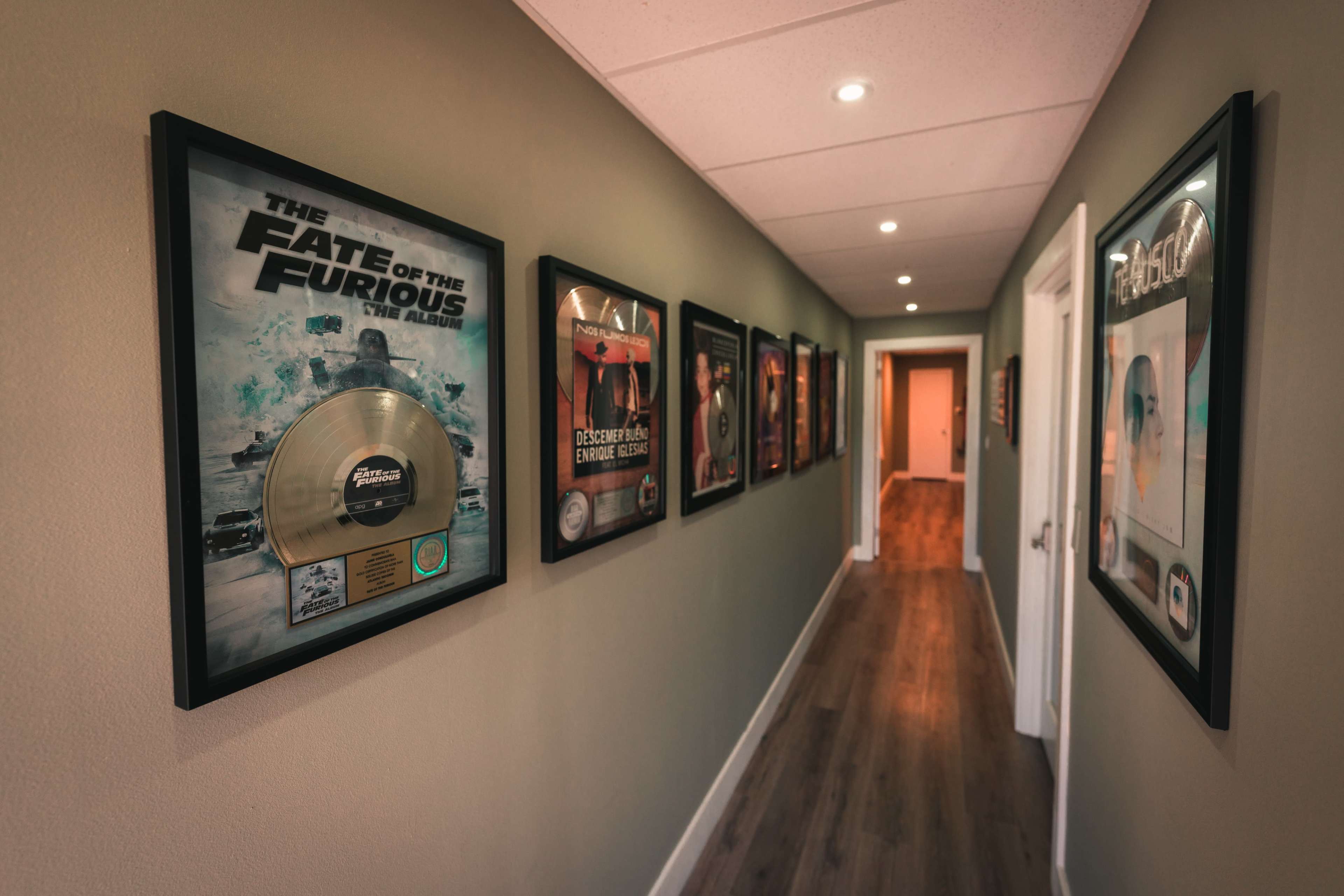 A hallway featuring framed music awards and movie posters along the walls, illuminated by overhead lights.