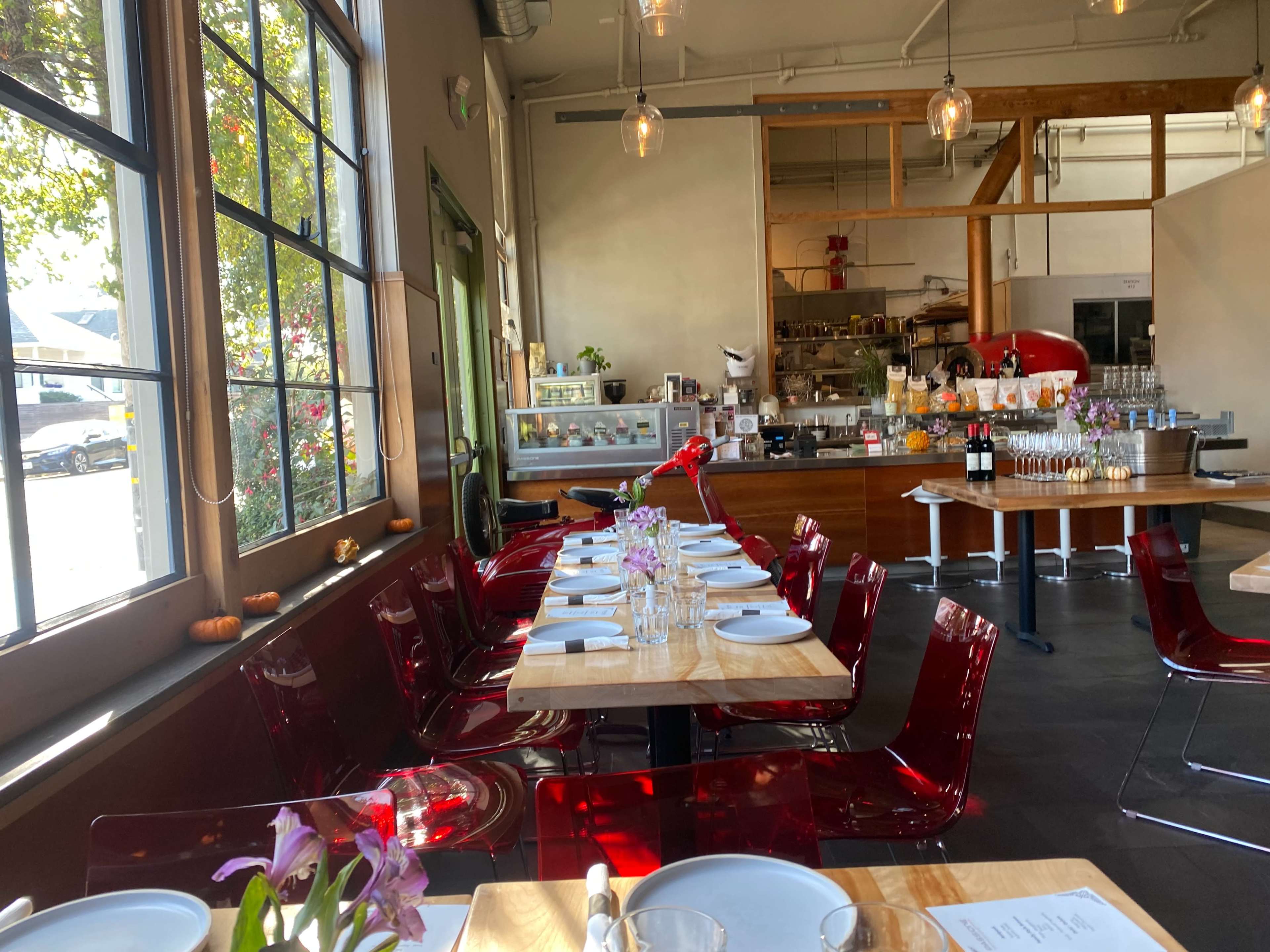 A modern restaurant interior features a long table set with white plates and purple flowers, with a visible bar and kitchen in the background.