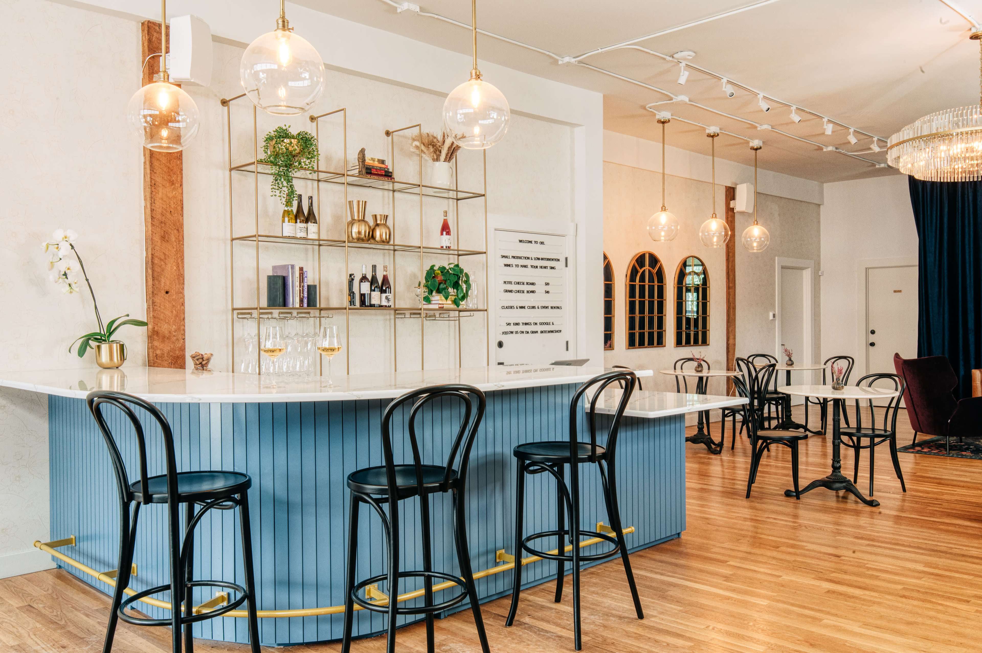 A modern bar area features a blue and white counter with black chairs, glass shelves displaying beverages, and elegant lighting fixtures.