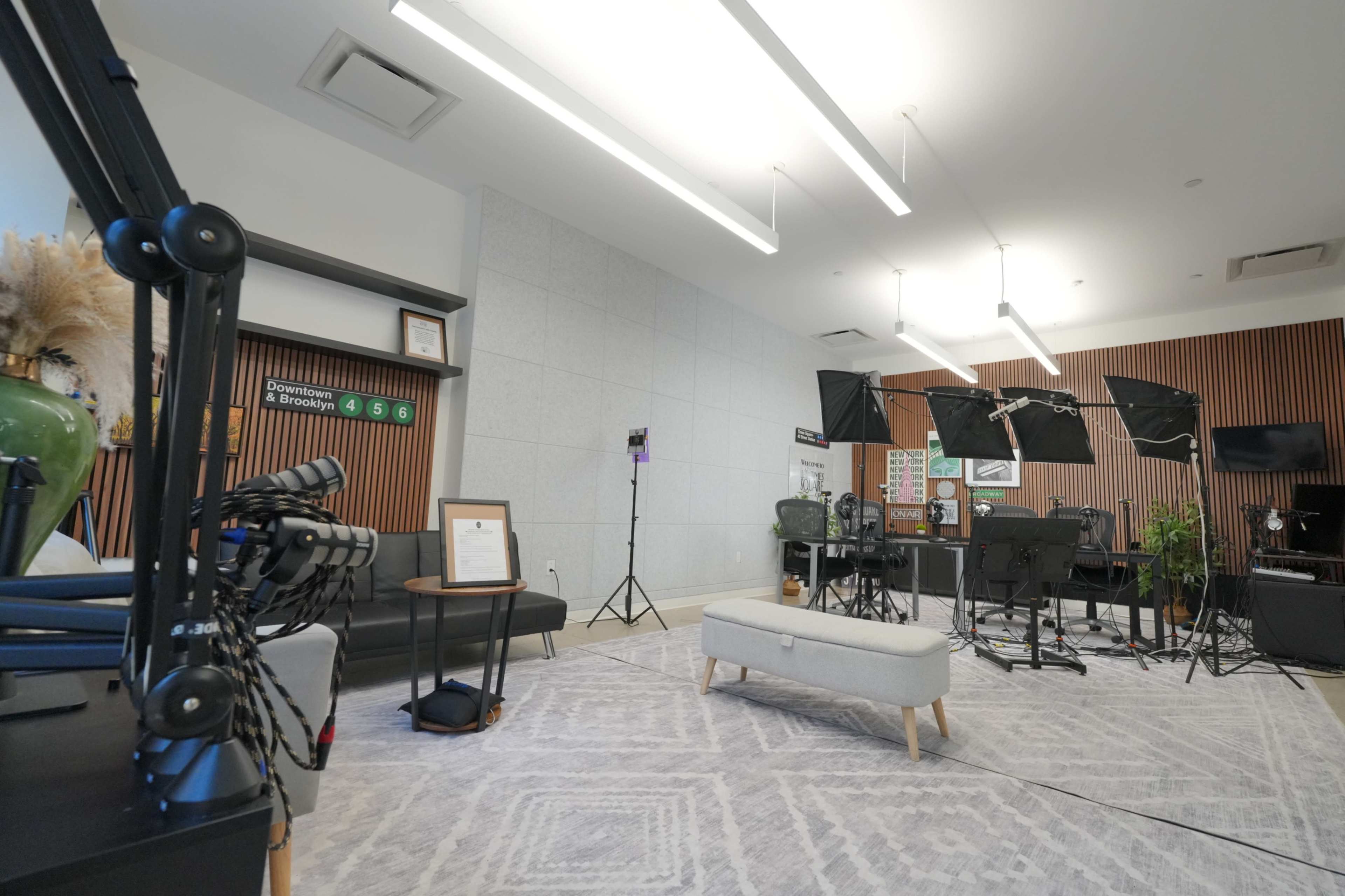 The image shows a modern office space equipped with cameras, lighting equipment, and various seating arrangements, accompanied by decorative plants and a notable wall design.