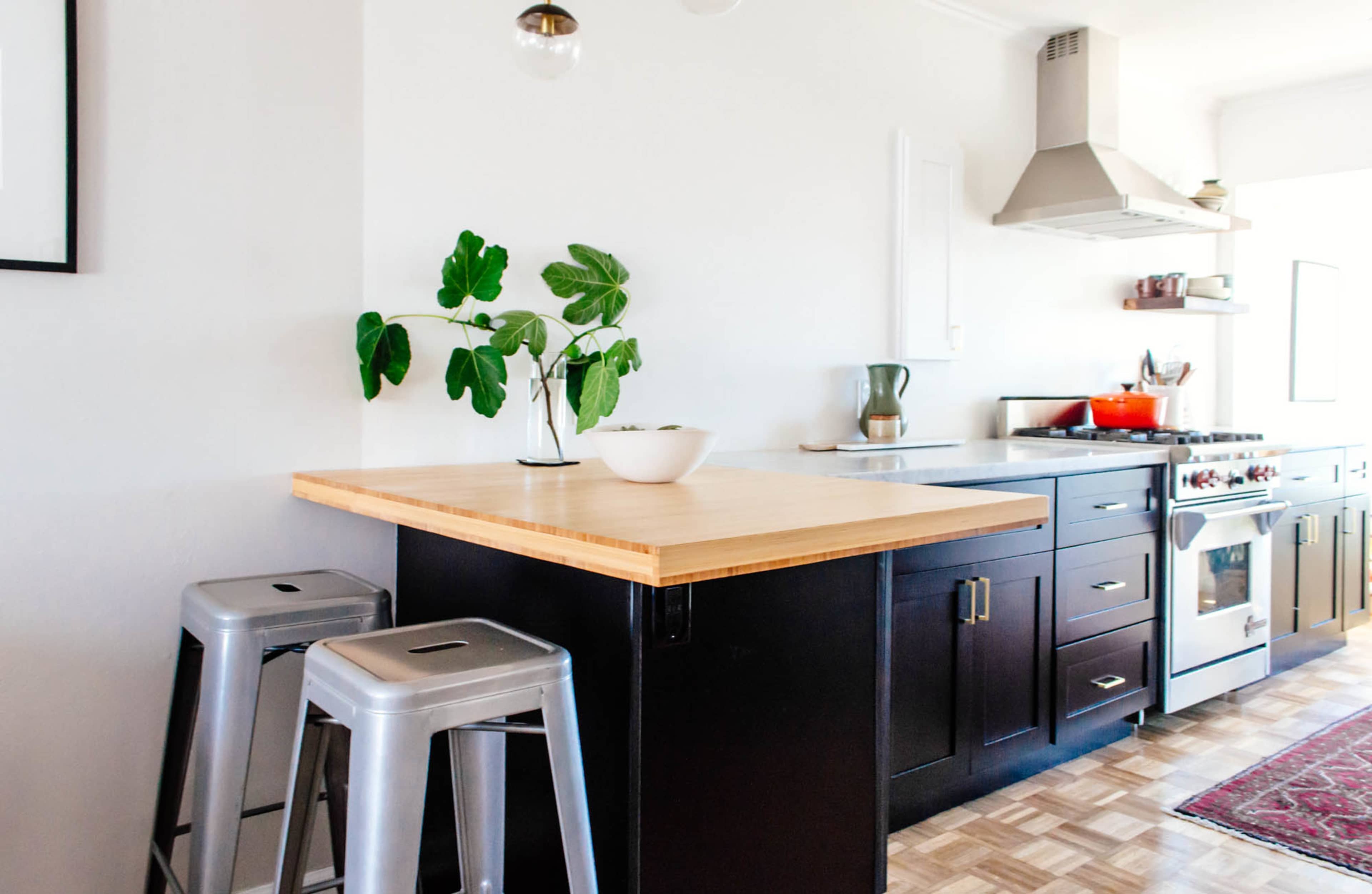 A modern kitchen with a wooden island, metal stools, and stainless steel appliances, including a stove and an exhaust hood.