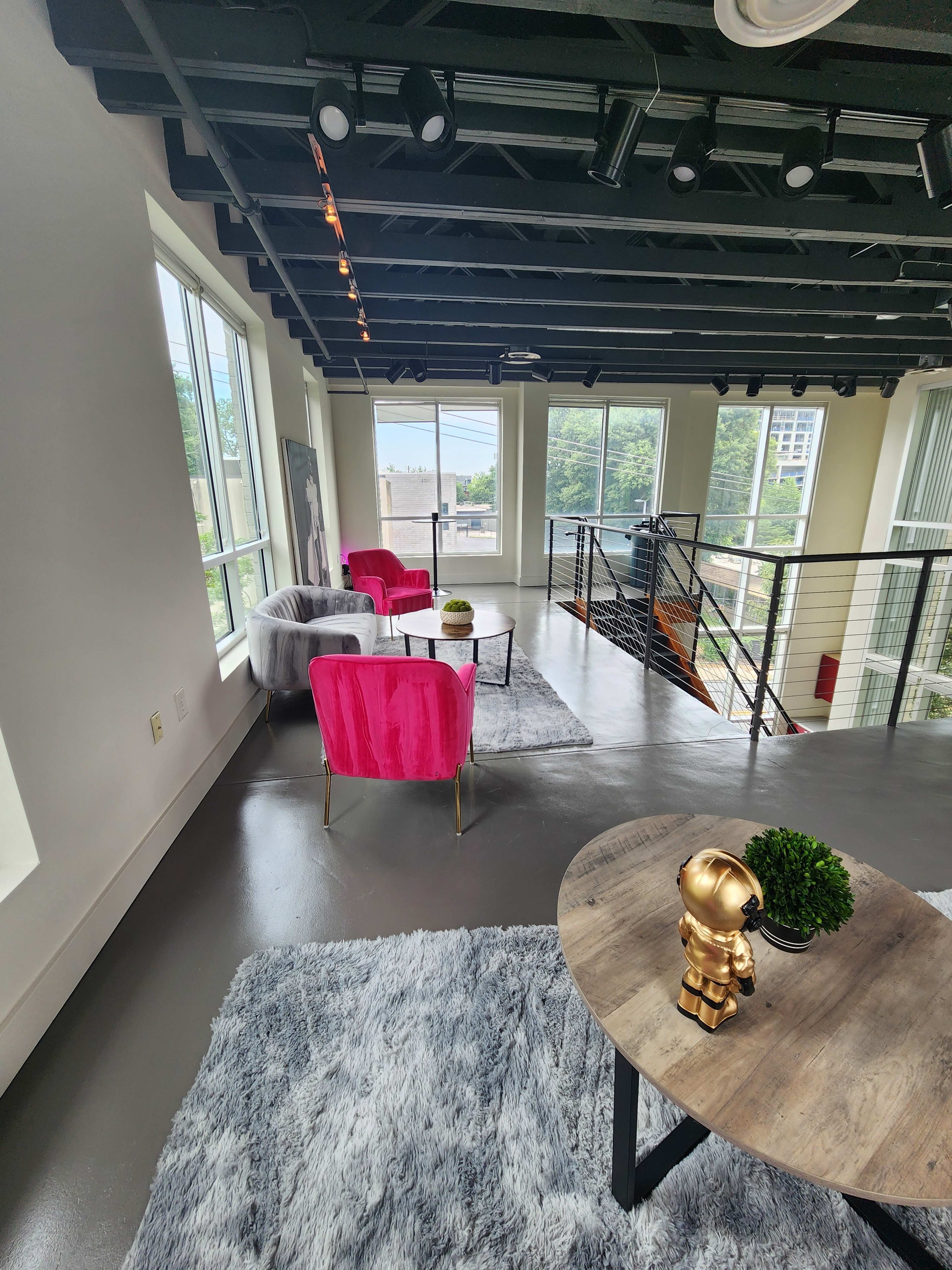 A modern loft space with two pink chairs, a gray rug, and a small table featuring a decorative plant and a golden figurine.