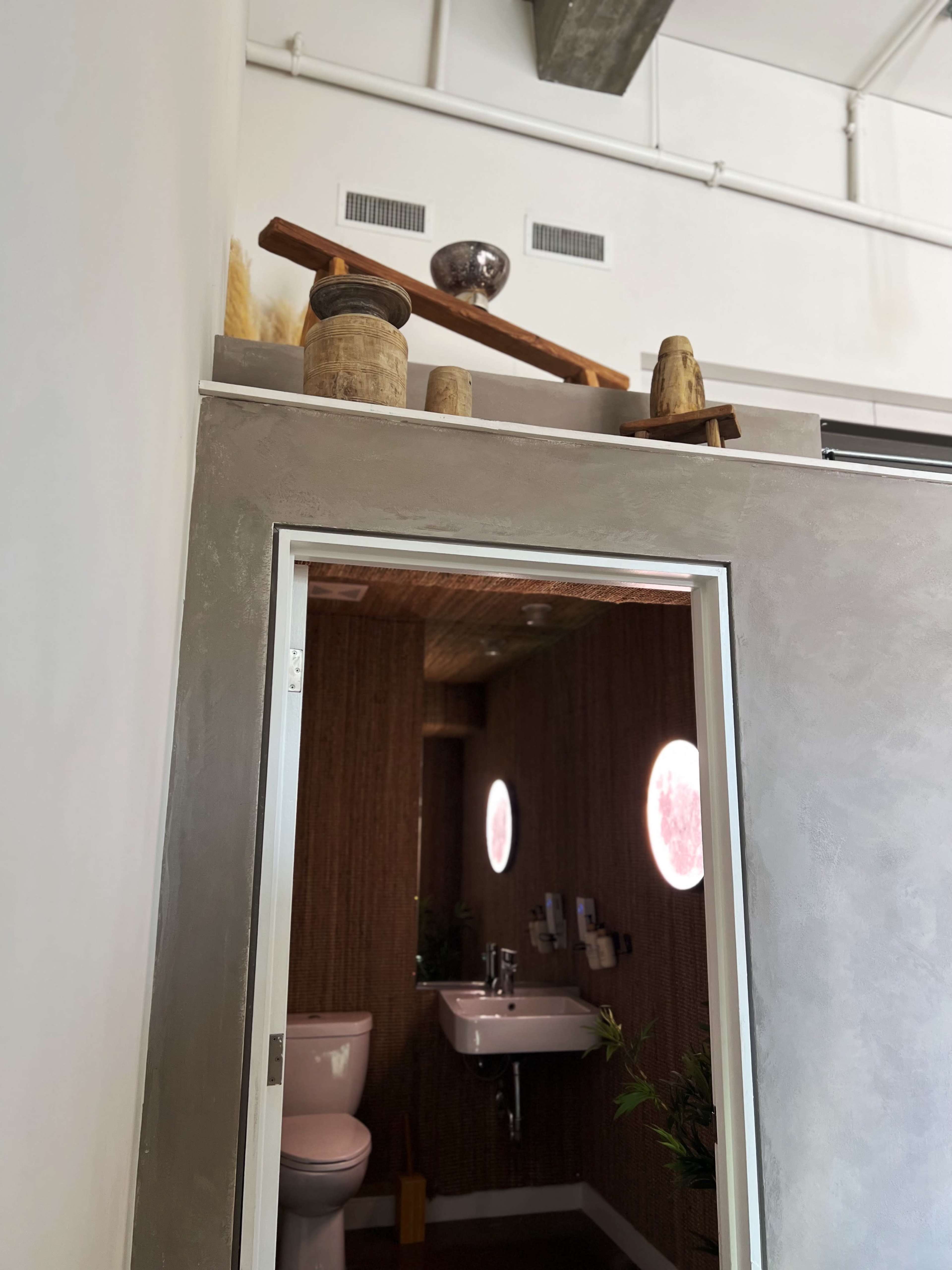 The image shows a modern restroom with a partially open door framed by a textured wall and decorative items displayed above it.