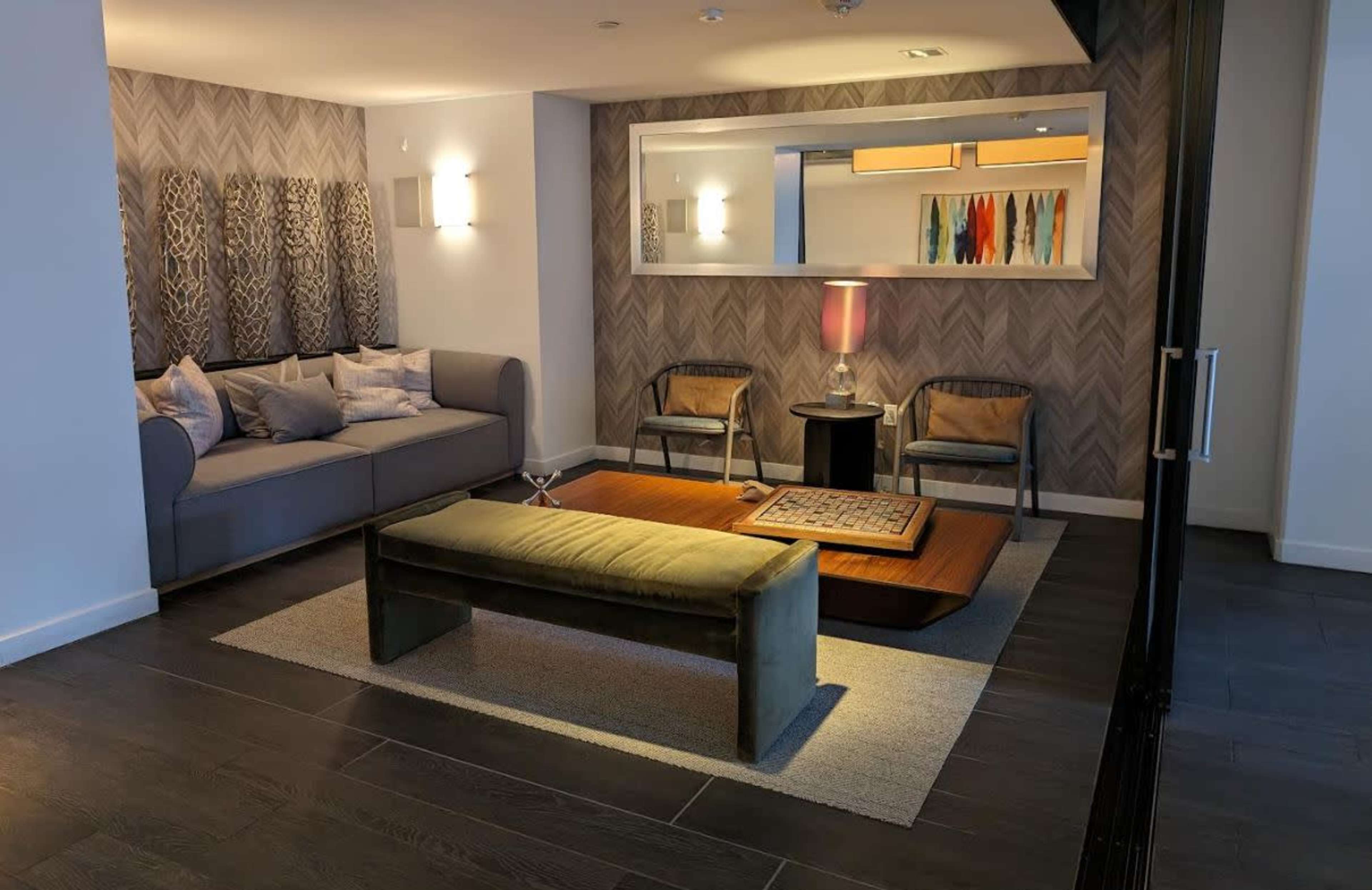 A modern living room with a gray couch, two chairs, a wooden coffee table, and a decorative wall mirror.