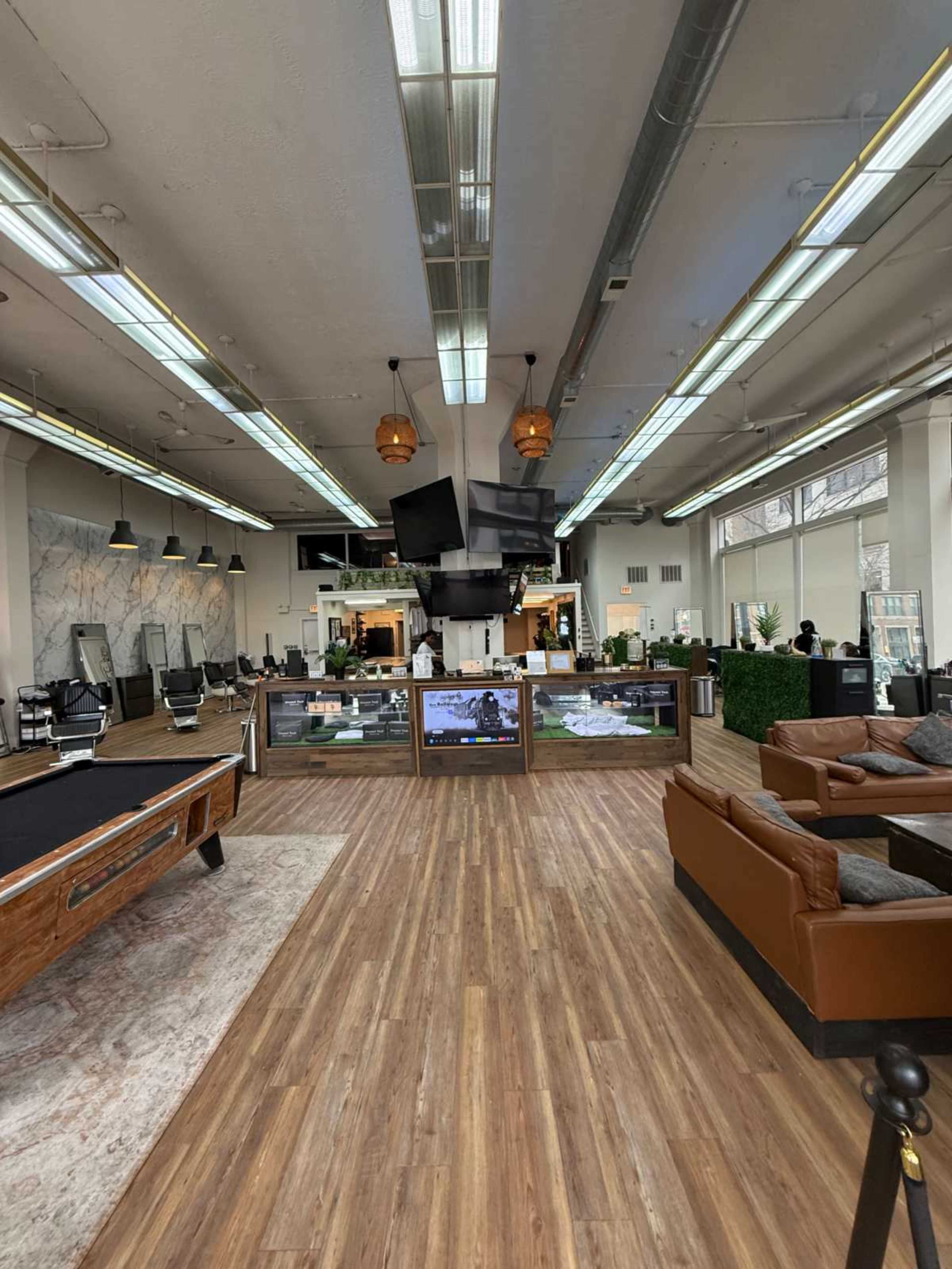 The image shows a spacious modern lounge area with a wooden floor, featuring a billiard table, leather seating, and large screens displaying content.