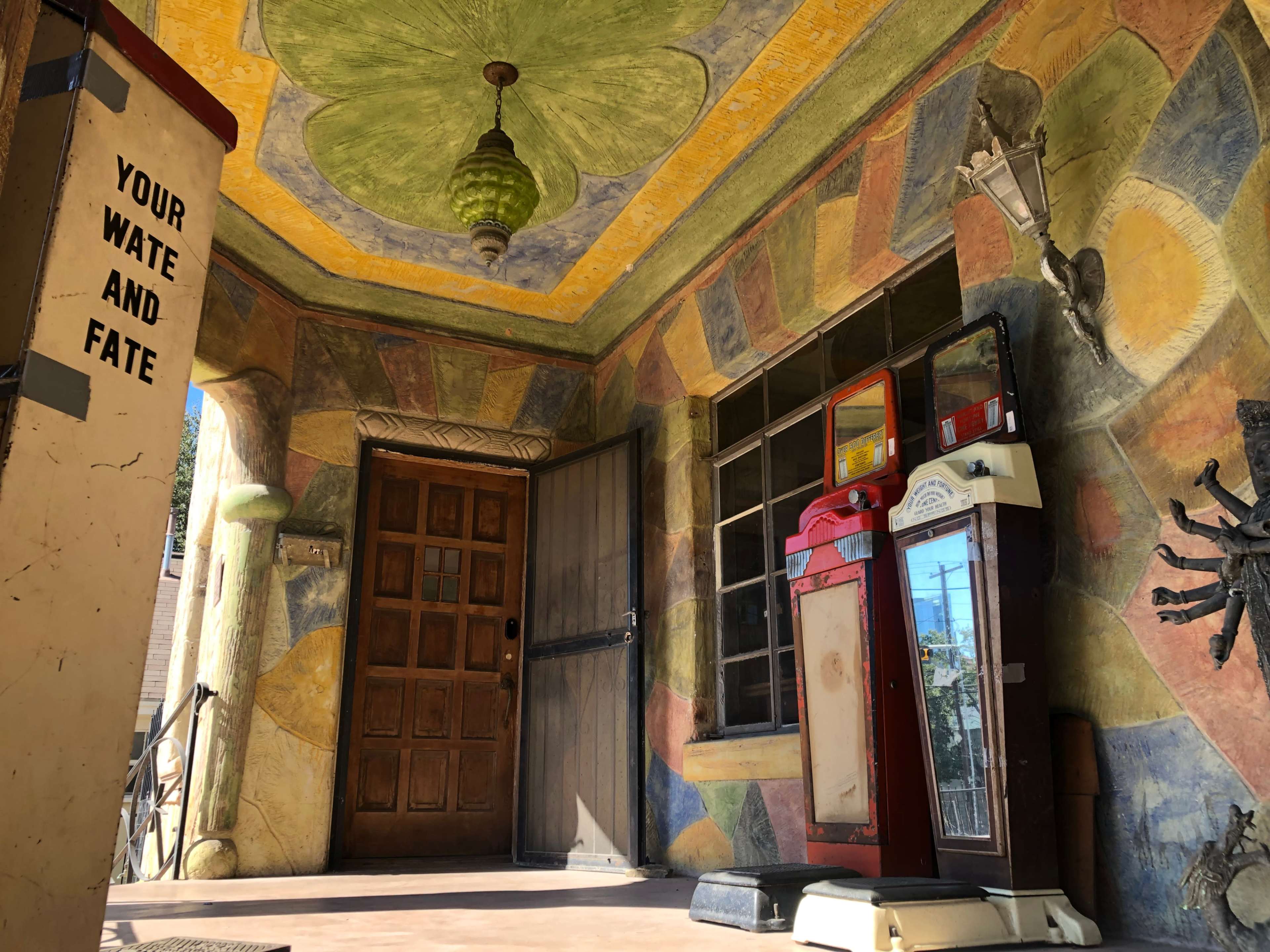 The image shows a vibrant, artistically painted entrance with a vintage gas pump and a wooden door.