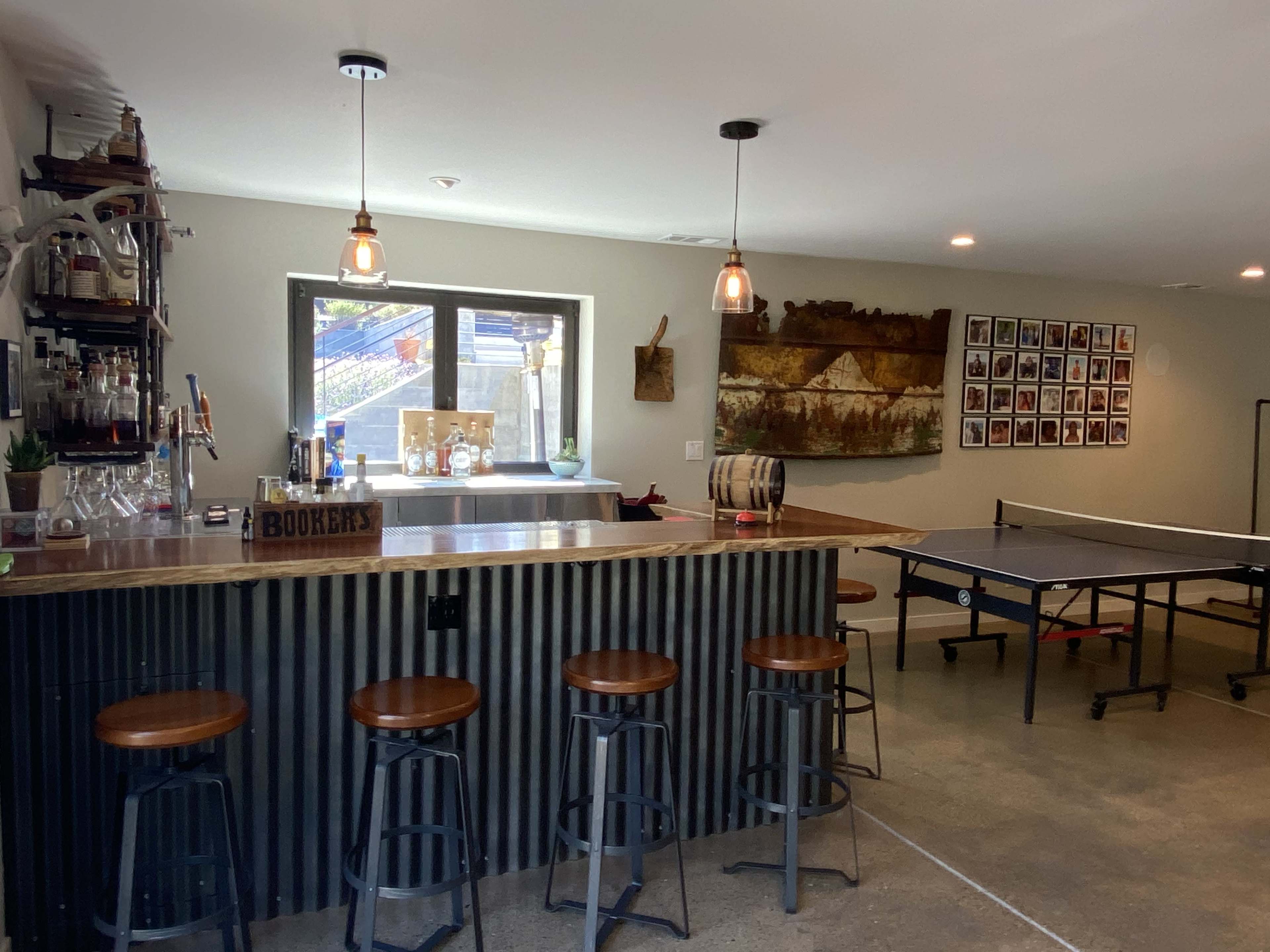 A modern, finished basement space featuring a bar with high stools, a ping pong table, and various artwork on the walls.