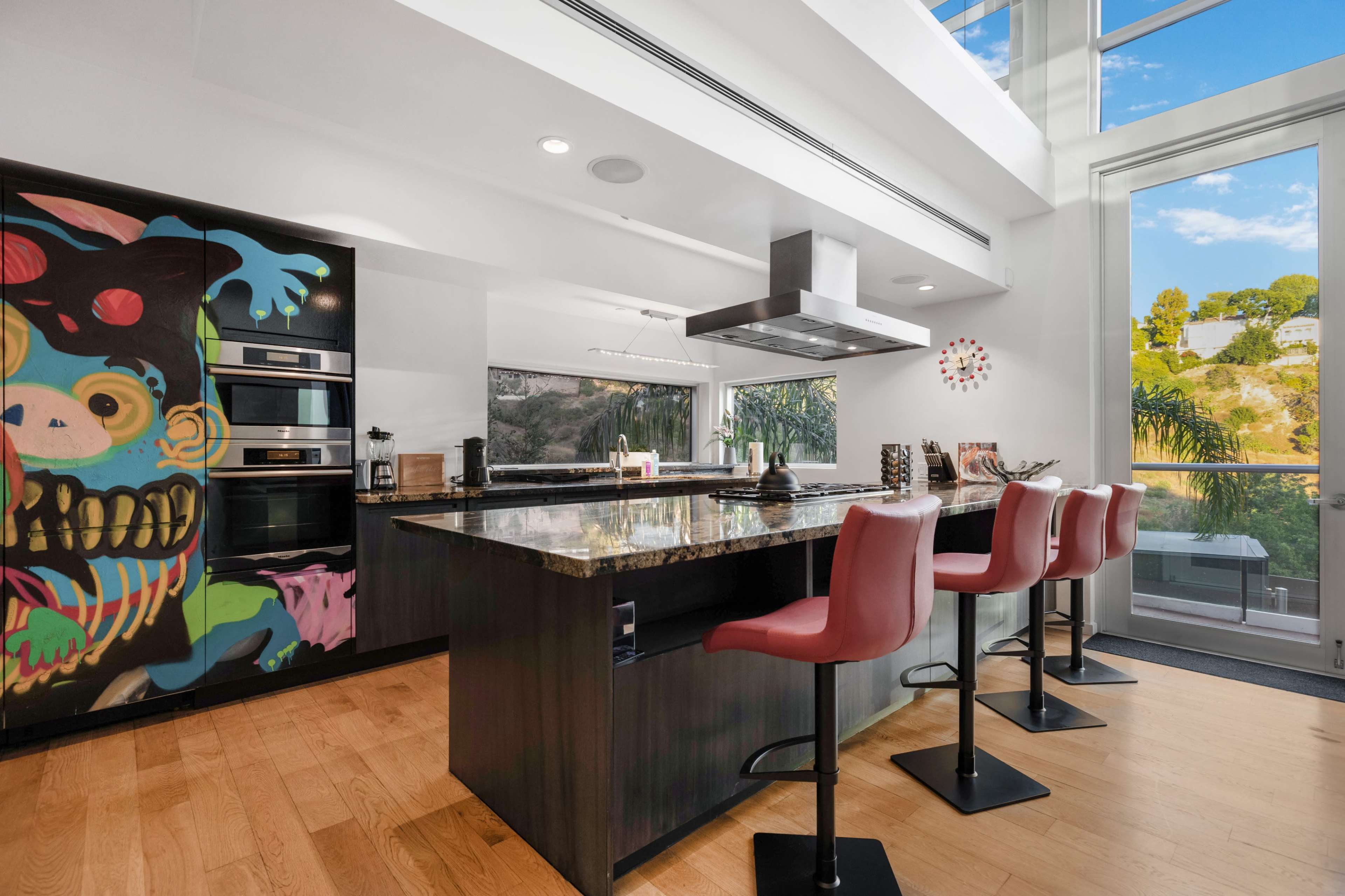 A modern kitchen features a large island with bar seating, sleek cabinets, and a vibrant mural on one wall.