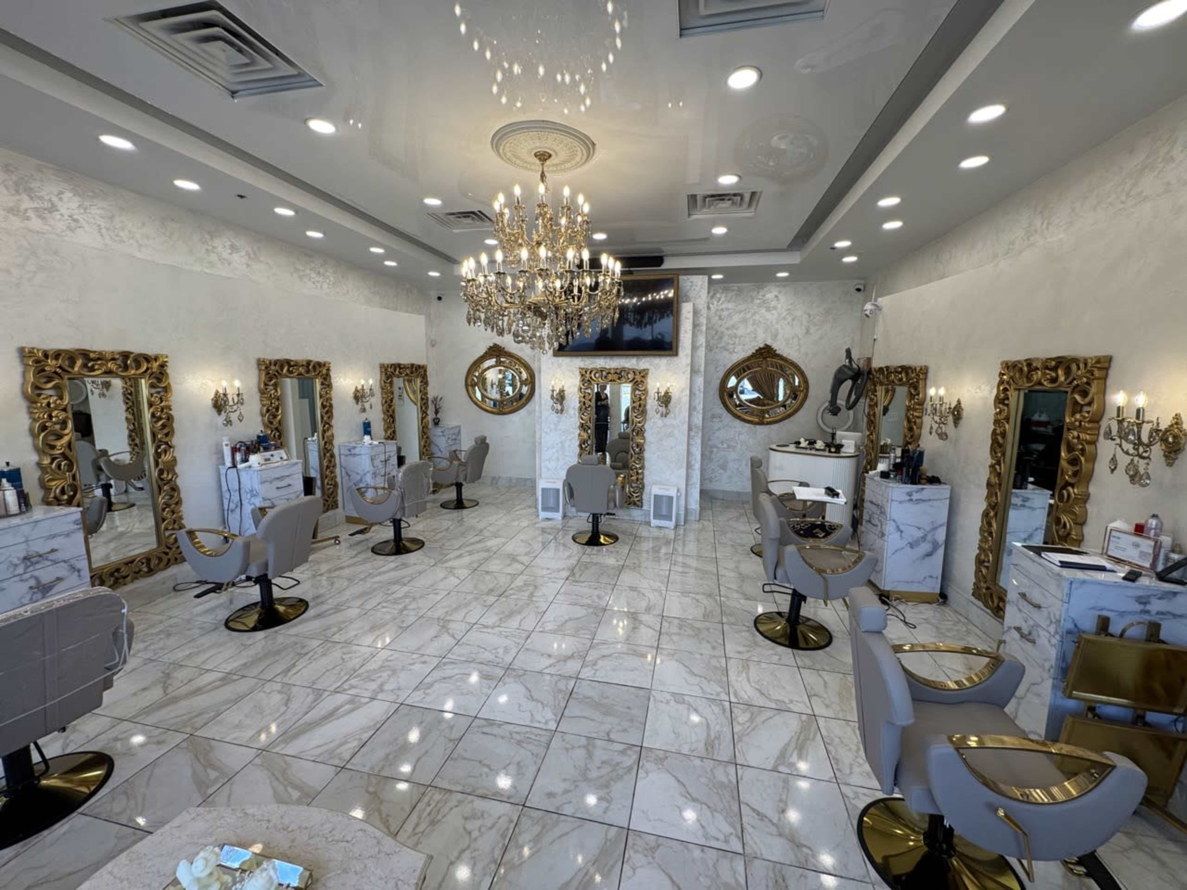 The image shows a spacious hair salon featuring elegant decor with golden mirrors, marble surfaces, and well-arranged styling stations under bright lighting.