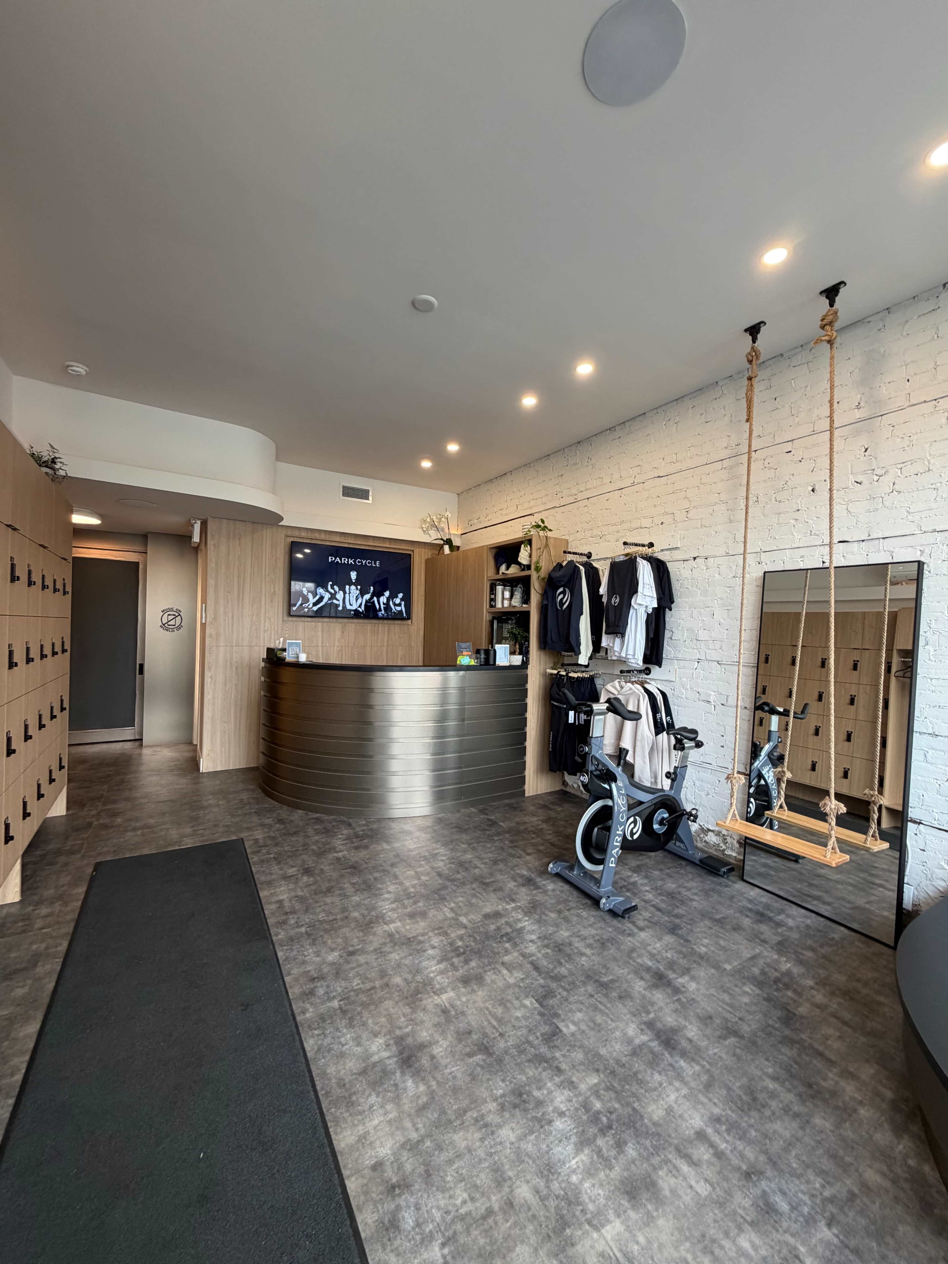 The image shows the interior of a fitness studio, featuring a reception desk, exercise equipment, clothing displays, and a large mirror.
