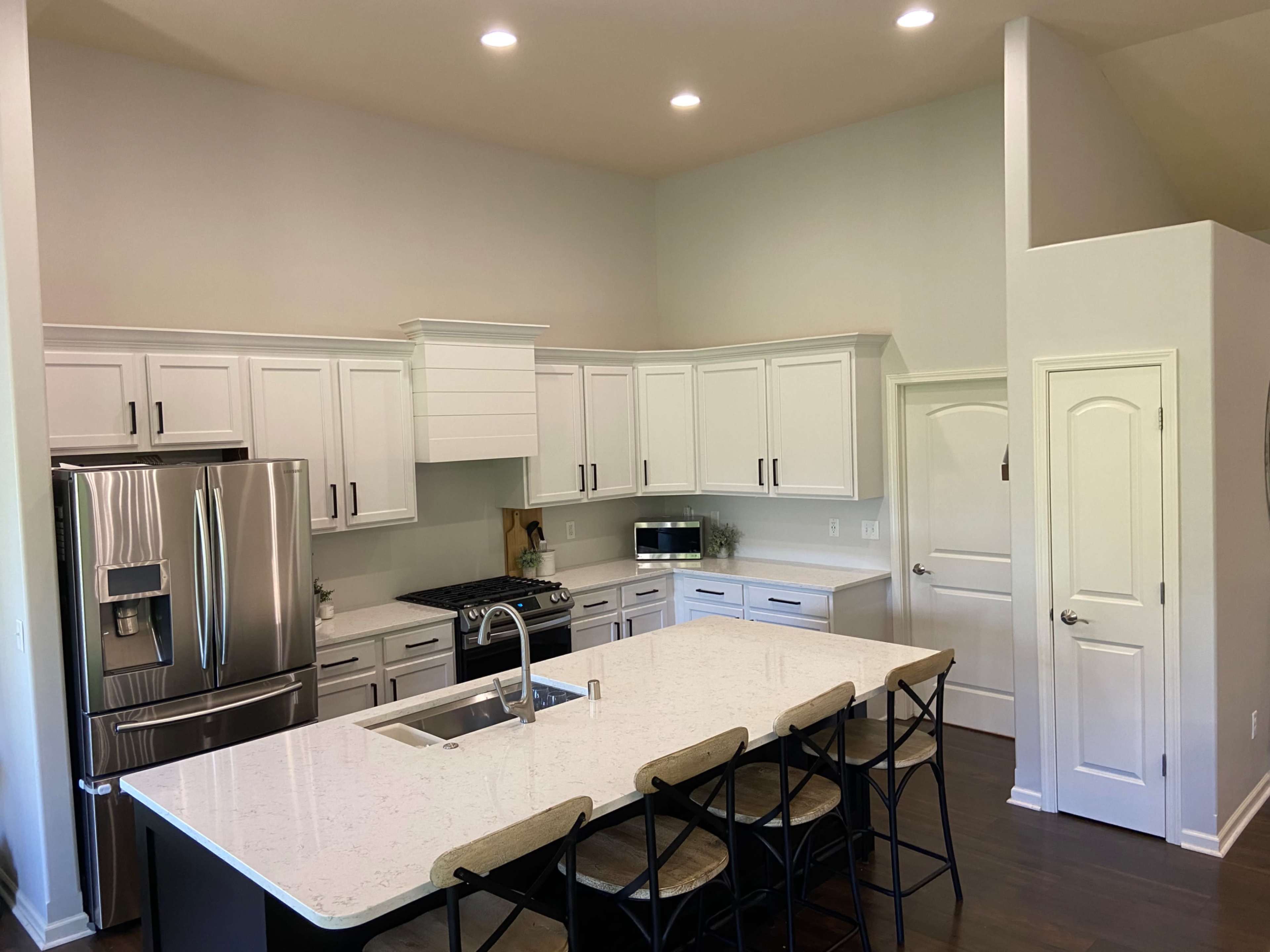 A modern kitchen features white cabinetry, a large island with seating, stainless steel appliances, and a gas stove.