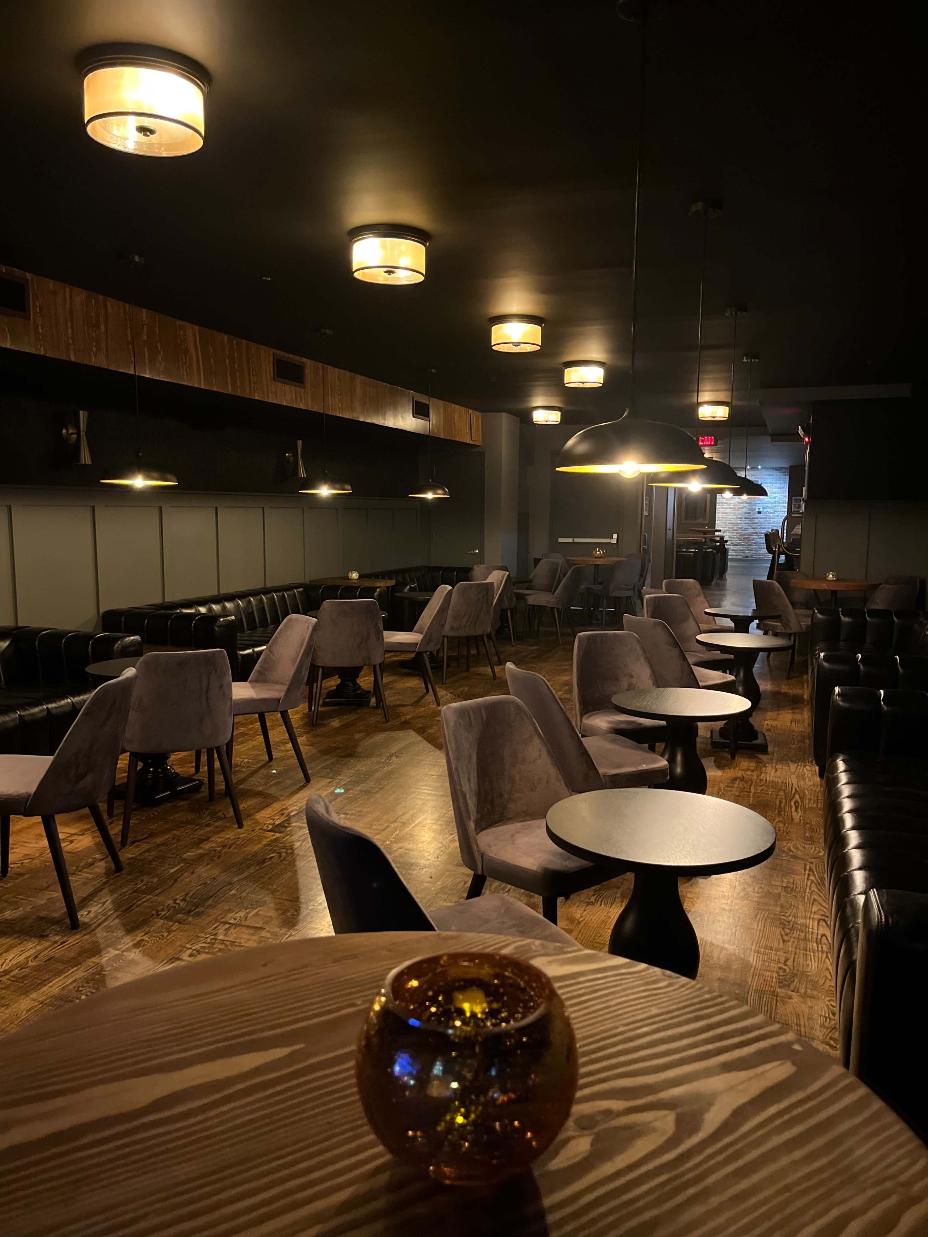 A dimly lit lounge with plush seating, small tables, and decorative lighting overhead.