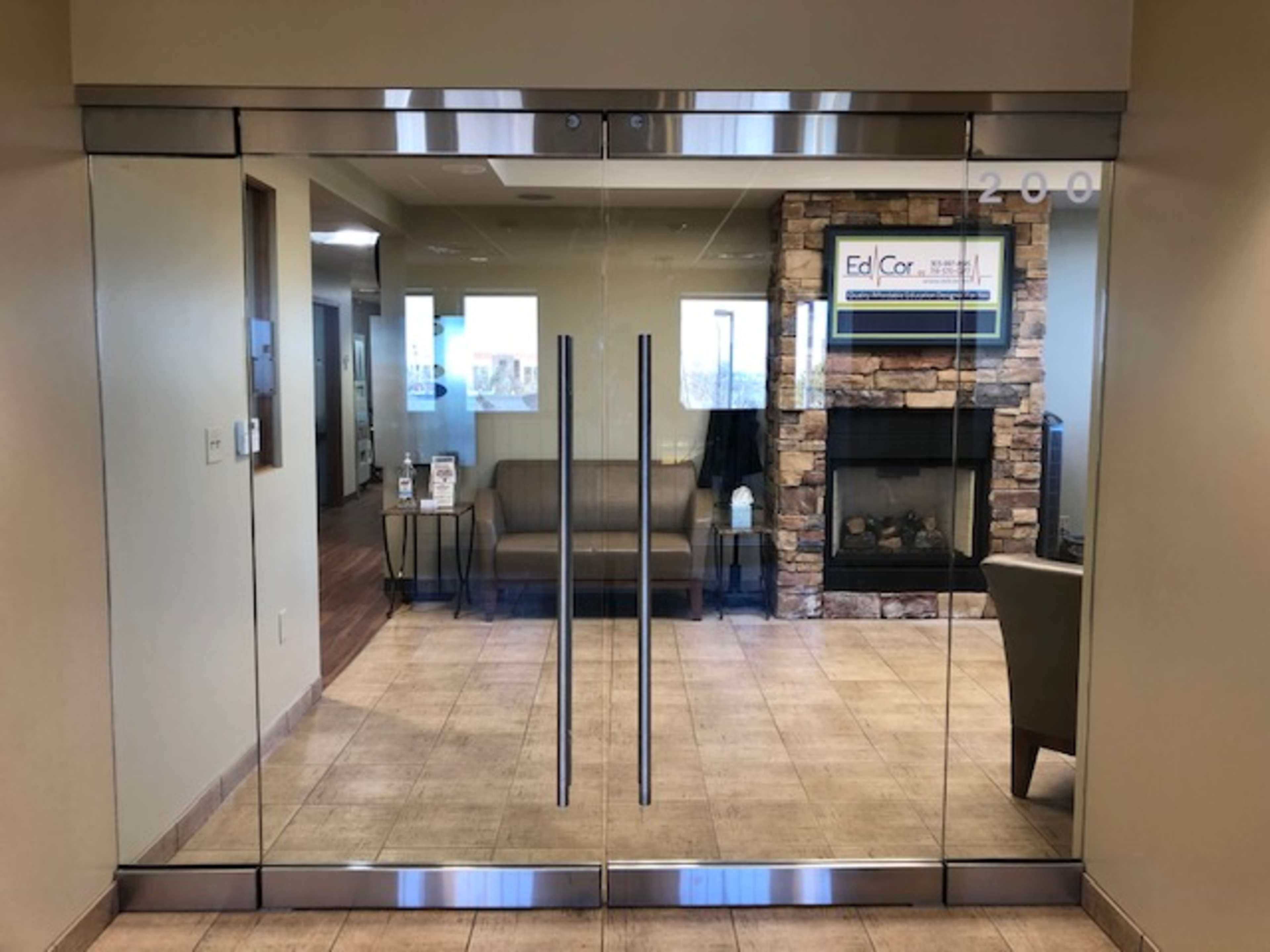 The glass entrance of an office with a waiting area featuring a sofa and a fireplace in the background.