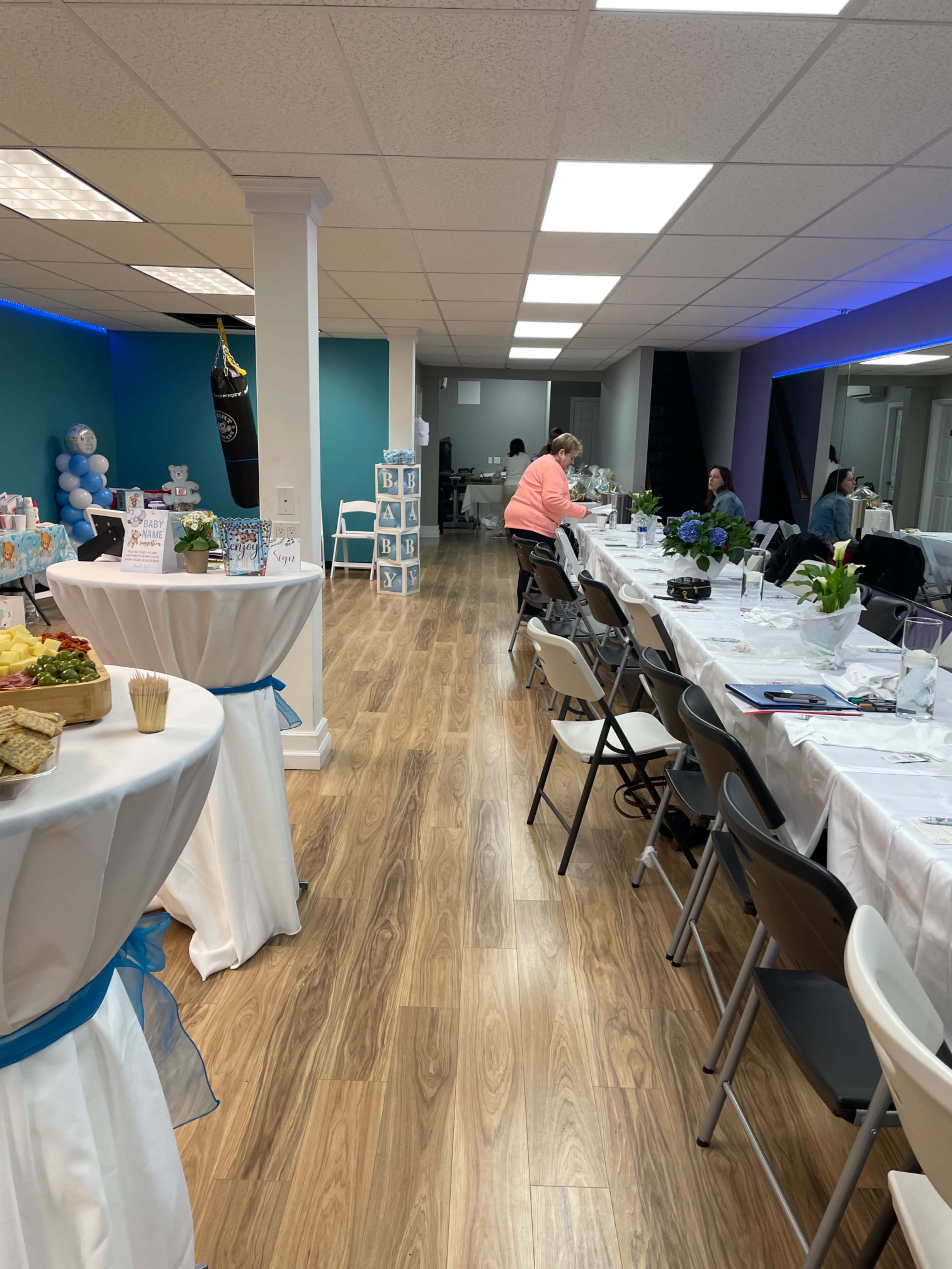 A well-decorated event space with tables set for a gathering and a person seated at one end.
