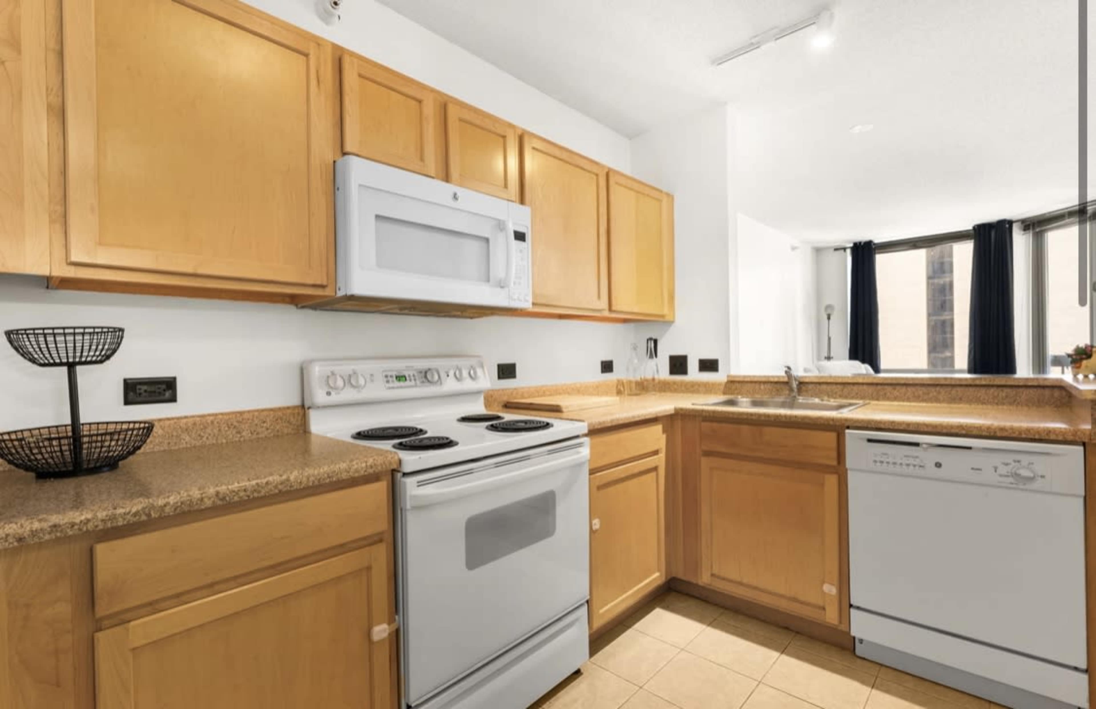 The image shows a modern kitchen with wooden cabinets, a stove, microwave, and dishwasher against a light-colored countertop.