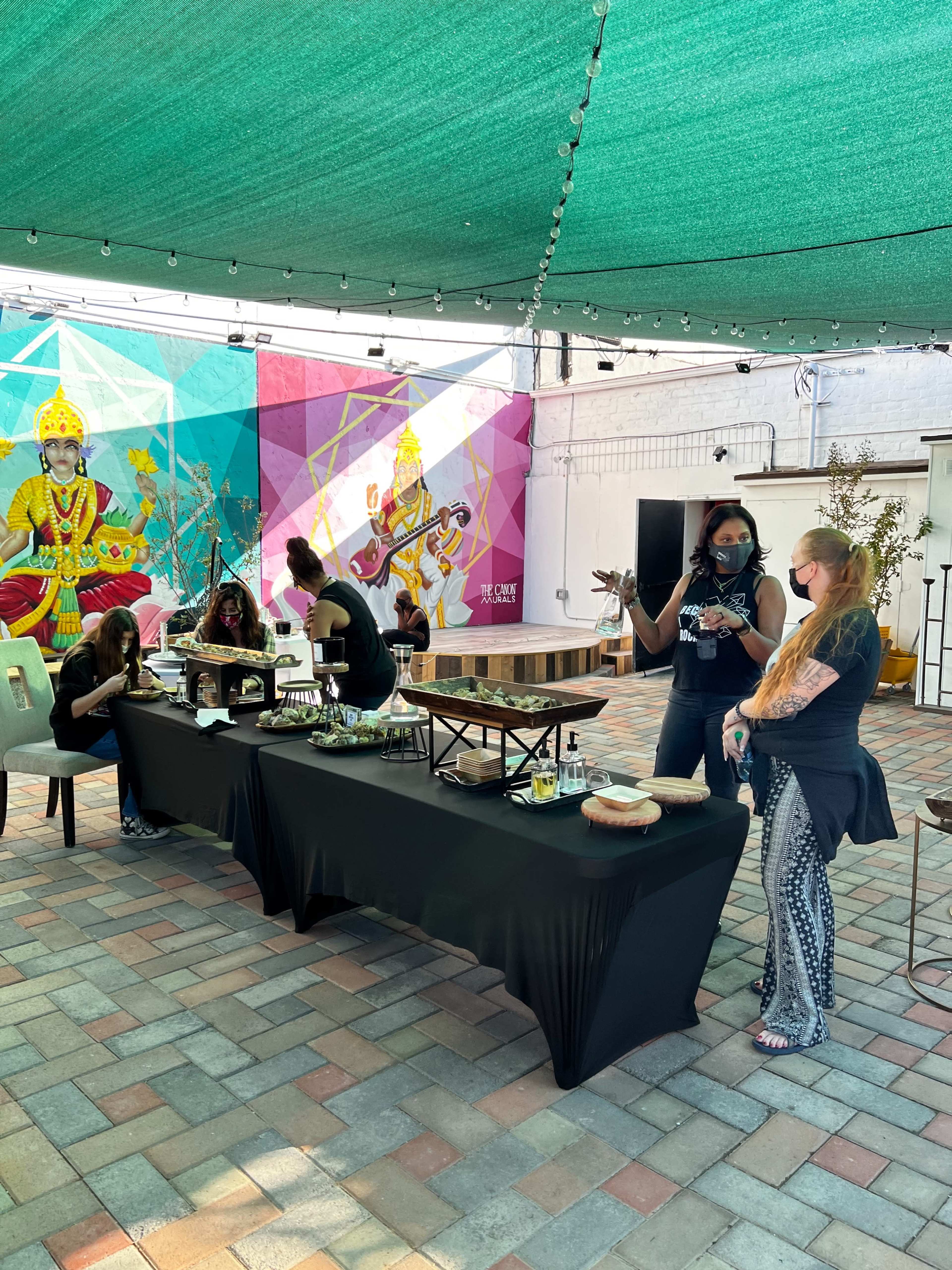 A group of people are engaged in various activities at a decorated outdoor venue with colorful murals in the background.
