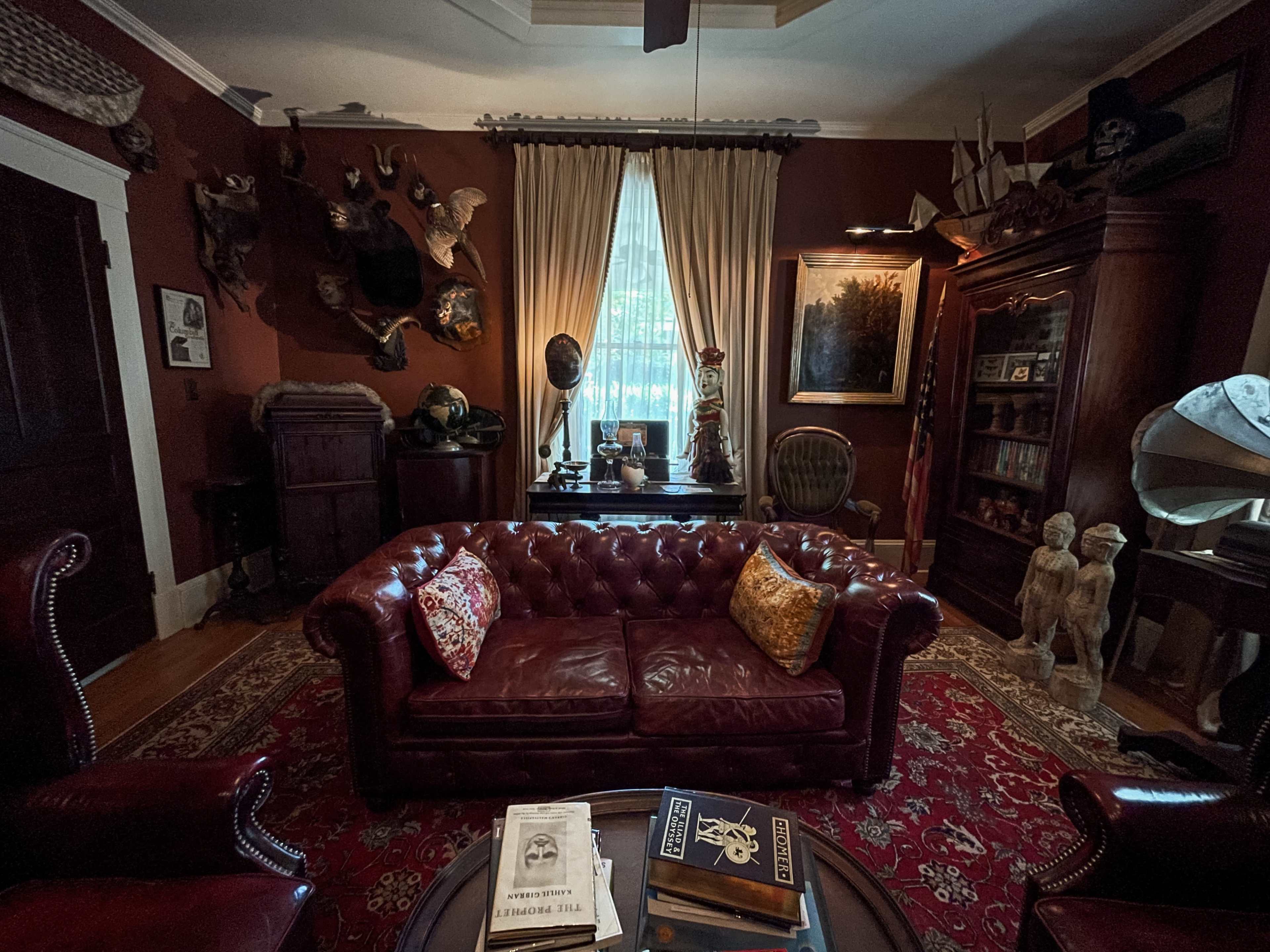 A room with dark red walls, featuring a leather couch, ornate furniture, and various taxidermy mounts and vintage decor.