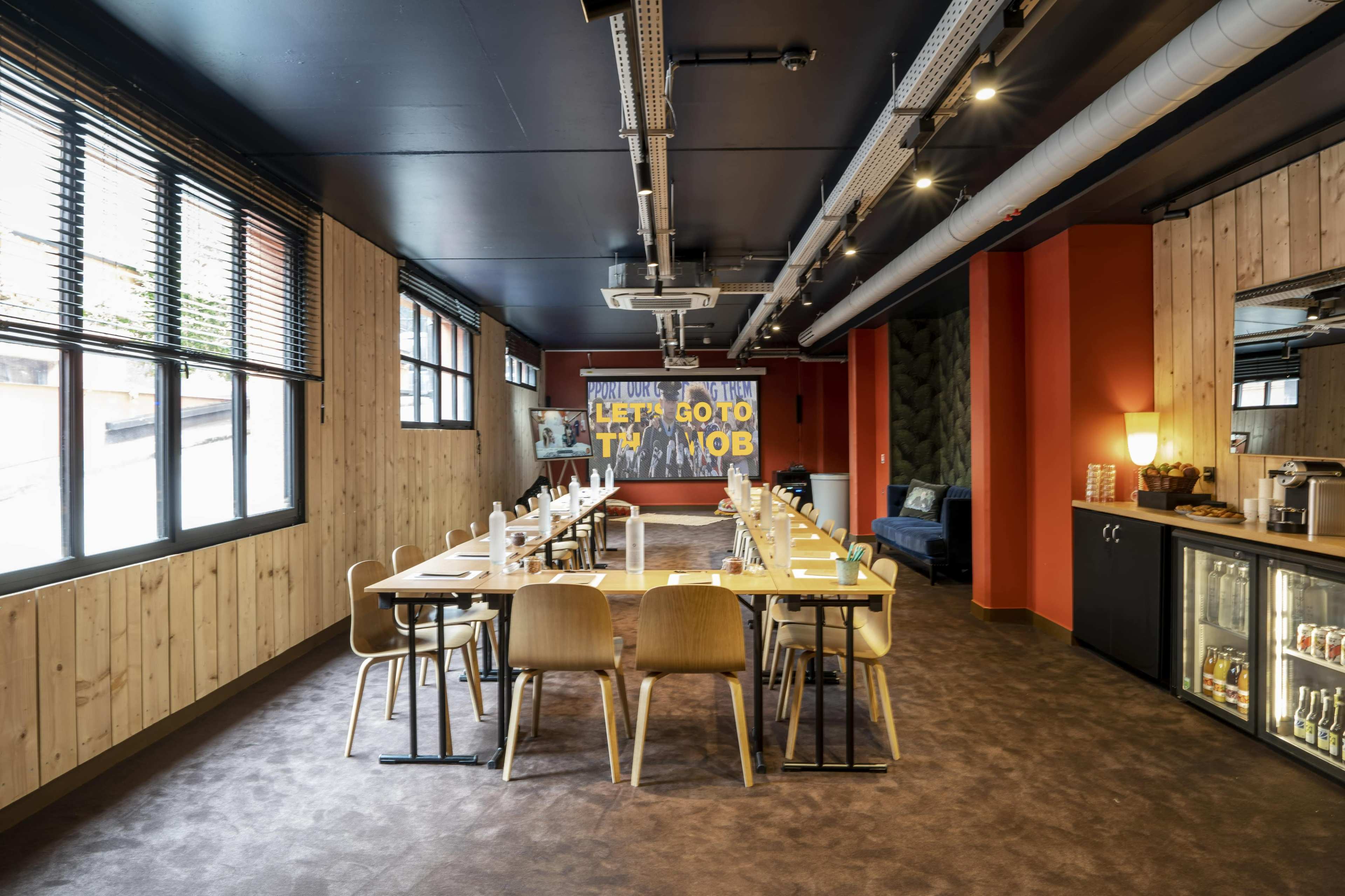 A modern restaurant interior featuring a long dining table, wooden paneling on the walls, and a colorful mural that reads "LET'S GO TO THE JOB."