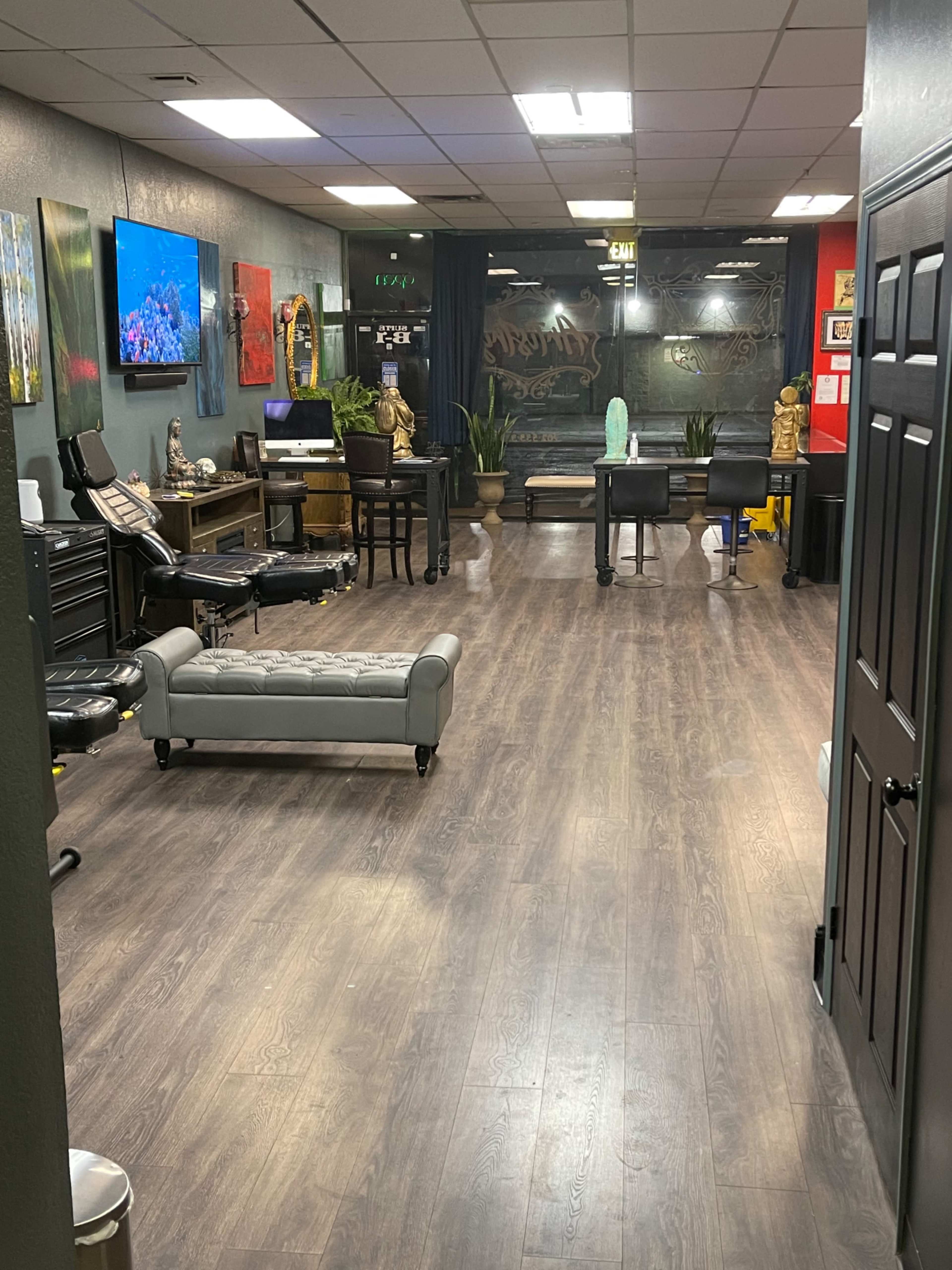 The interior of a tattoo studio with several workstations, chairs, and a large television mounted on the wall.