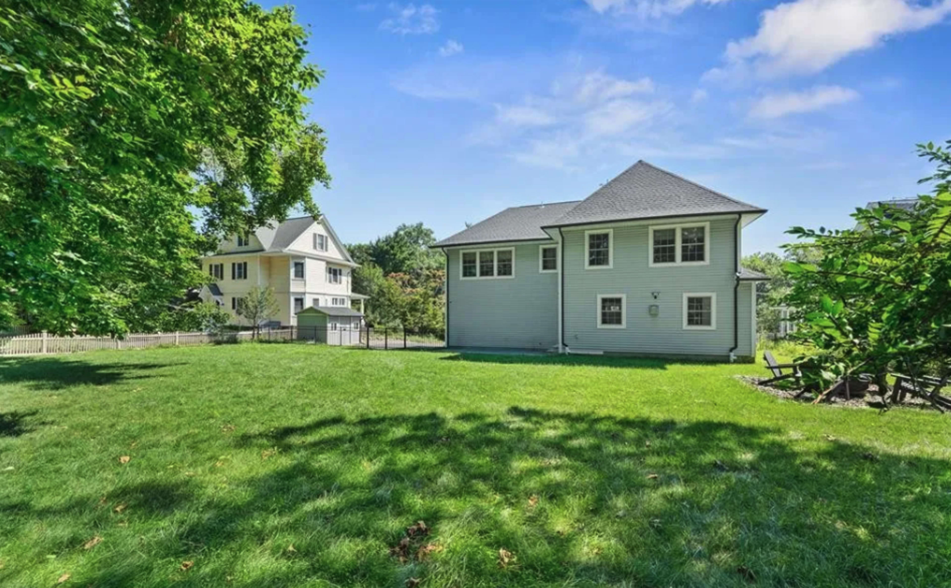 The image shows a green lawn with a gray house on the right and another house visible in the background on the left.