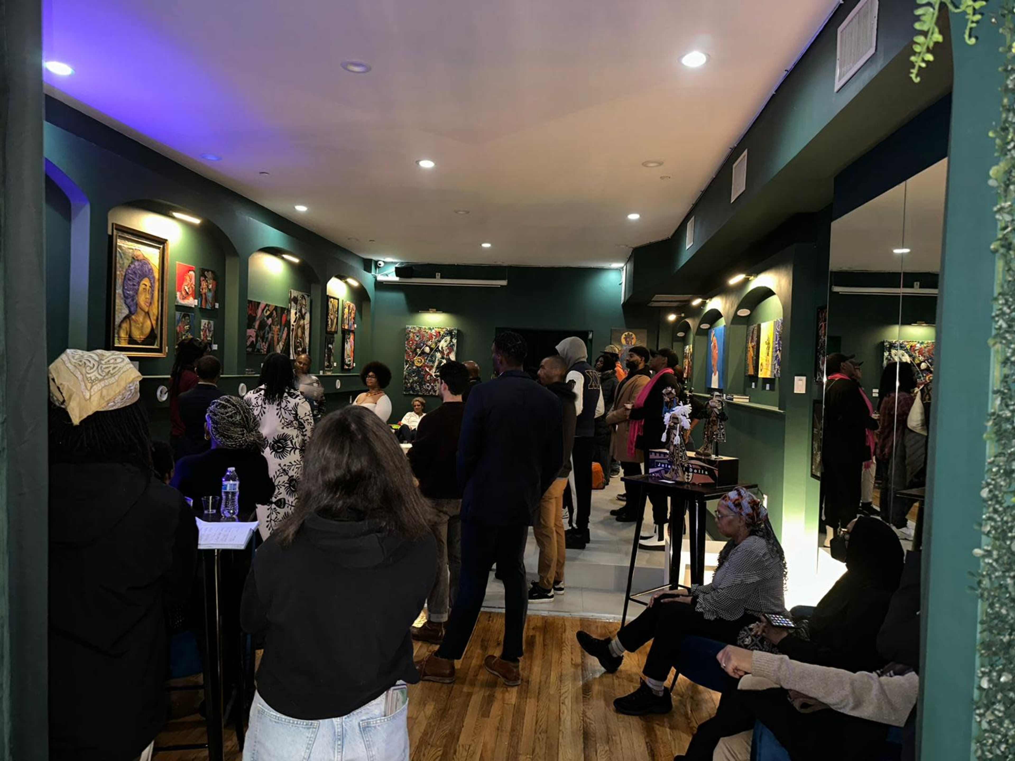 A crowd of people stands in an art gallery, admiring colorful paintings displayed on the walls.