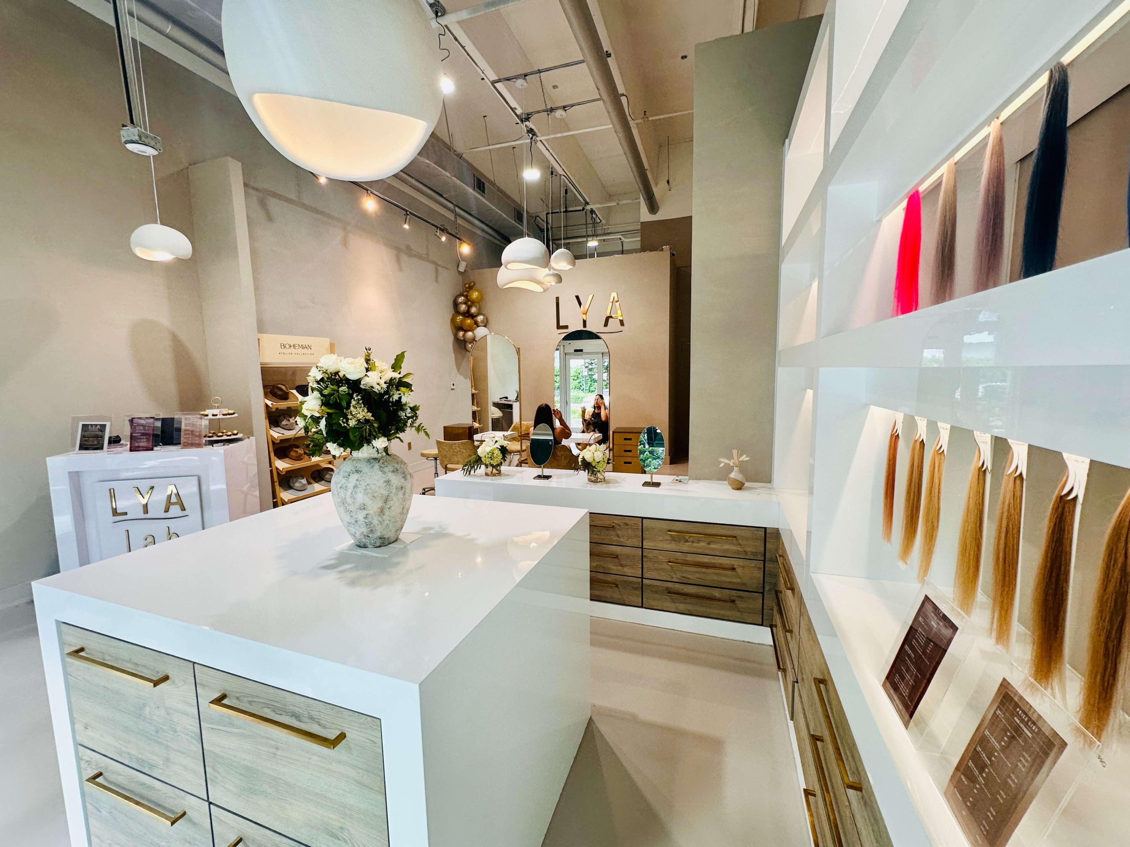 The image shows a modern salon interior featuring a white reception desk, display shelves with hair extensions, and elegant decor.