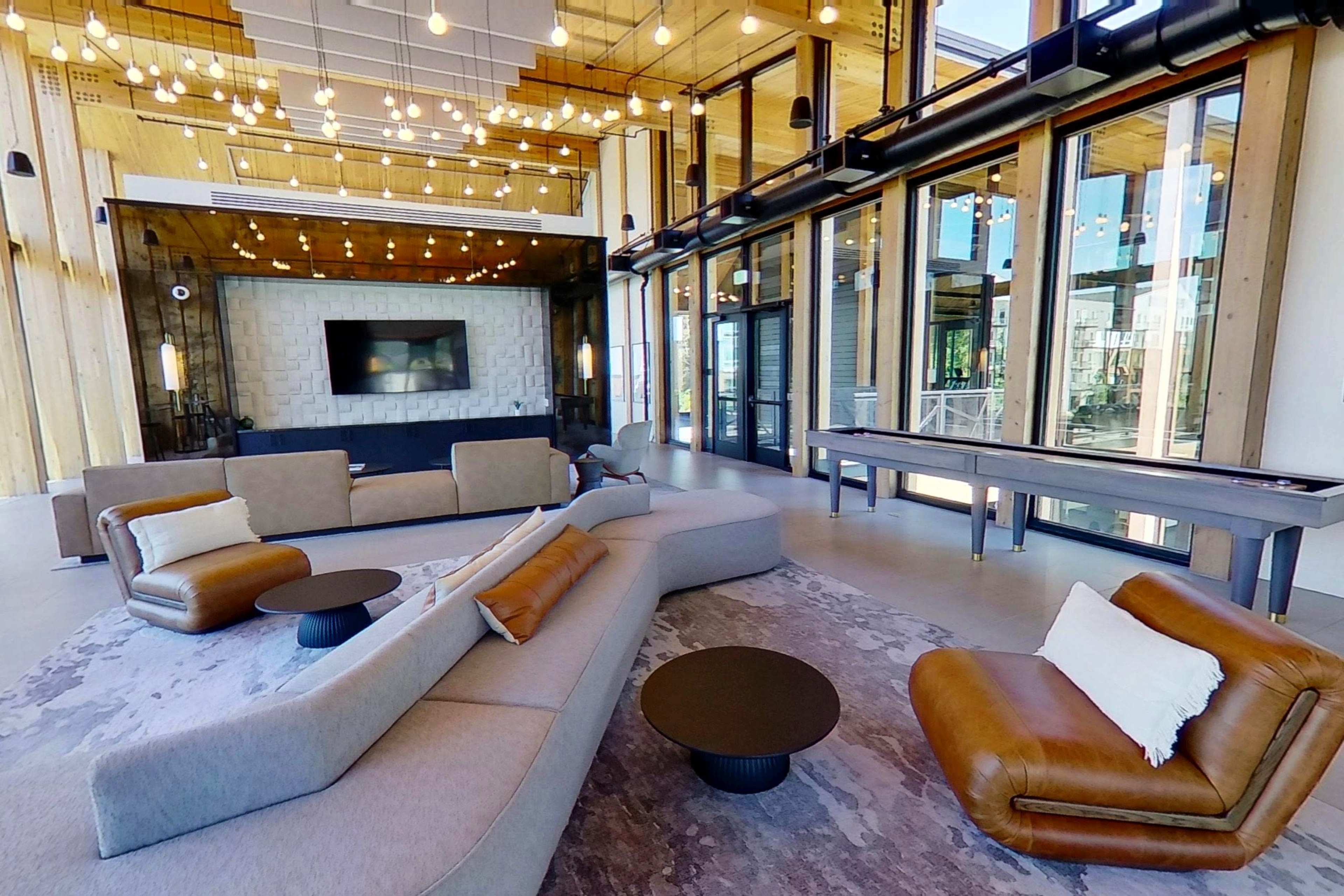 The image shows a modern lounge area with large windows, contemporary furniture, and decorative lighting.