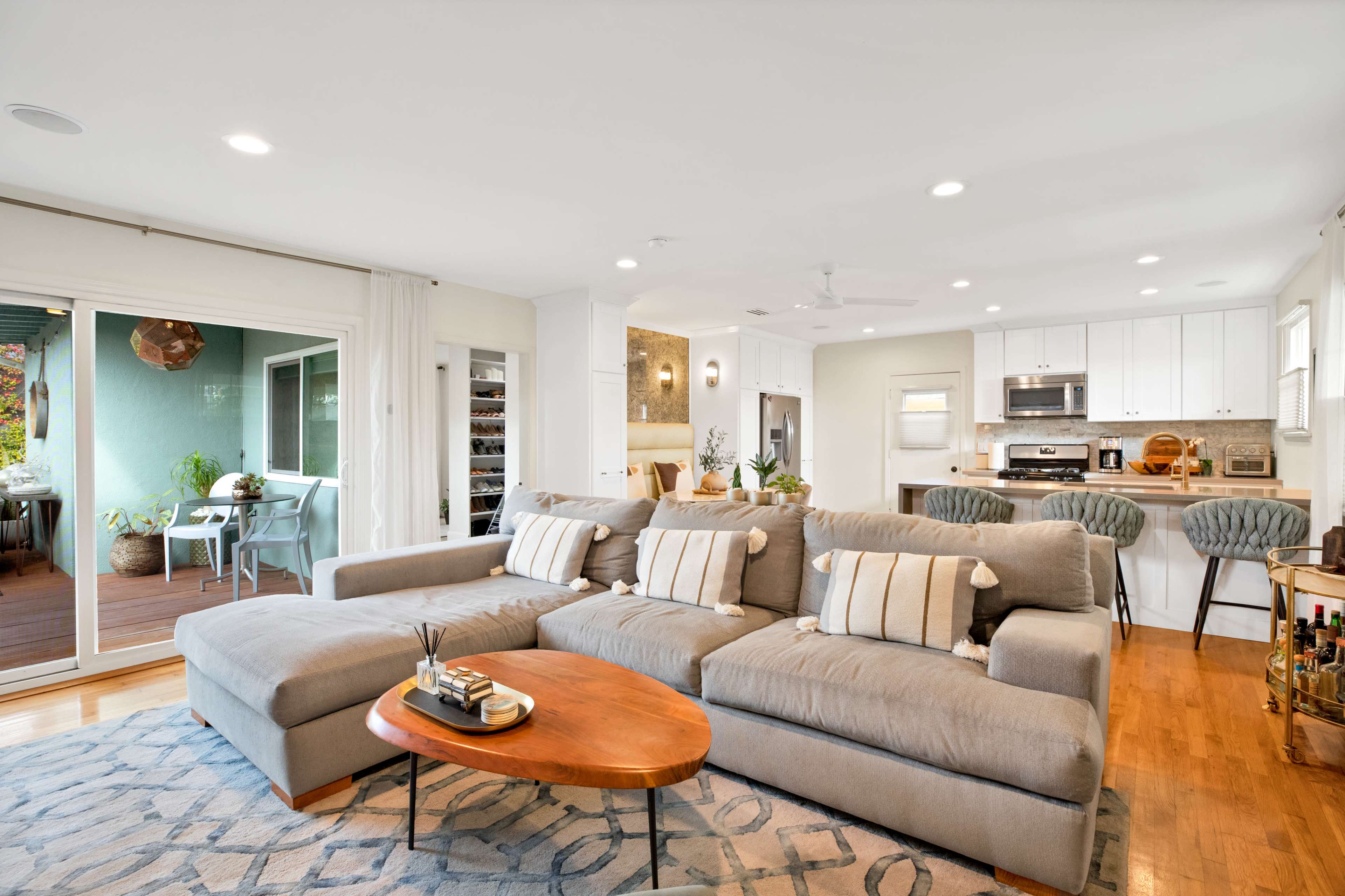 A modern living room features a gray sectional sofa, a wooden coffee table, and an open layout leading to a kitchen and dining area.