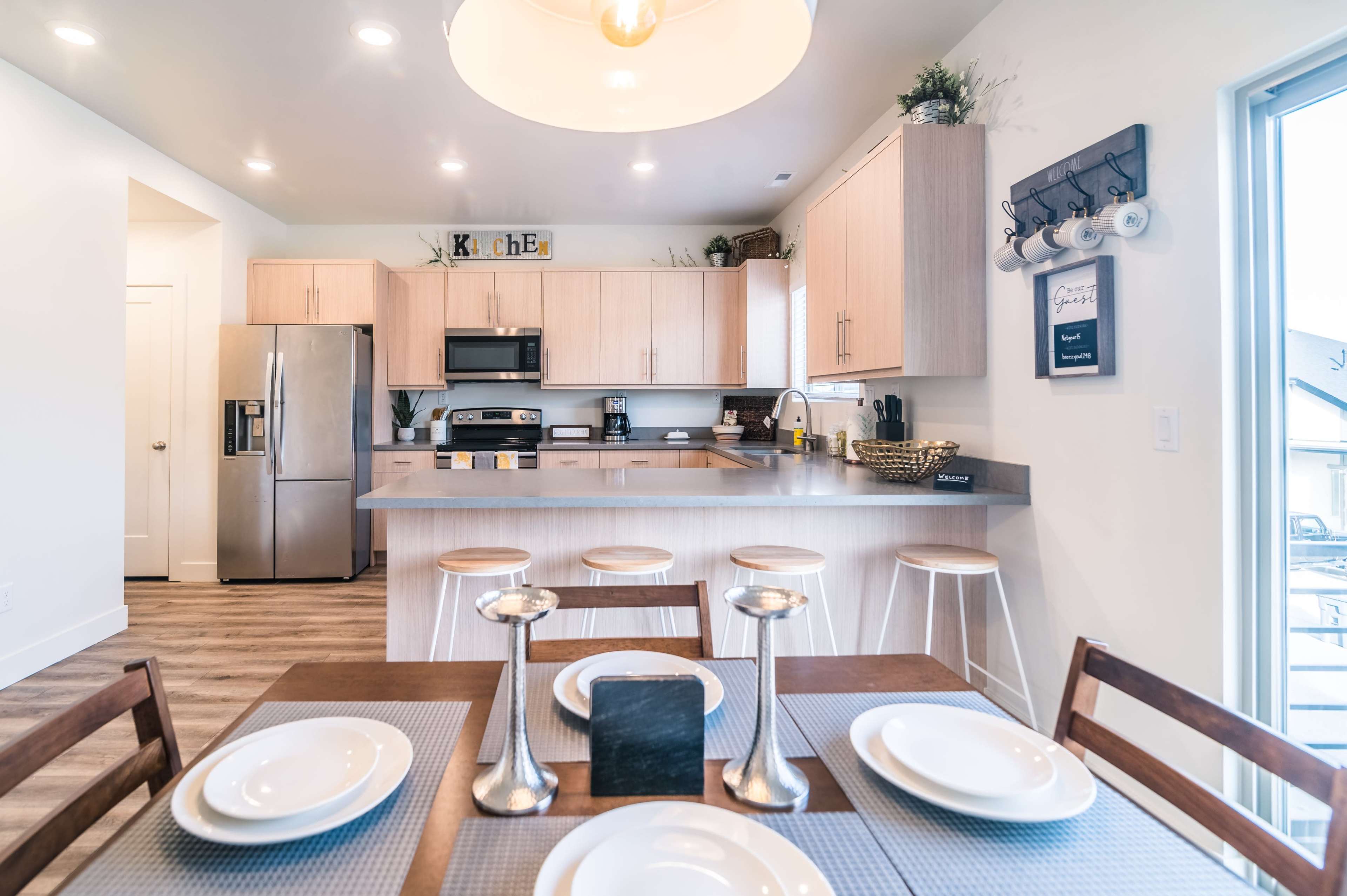 A modern kitchen features light wood cabinets, stainless steel appliances, and a dining area with a table set for a meal.