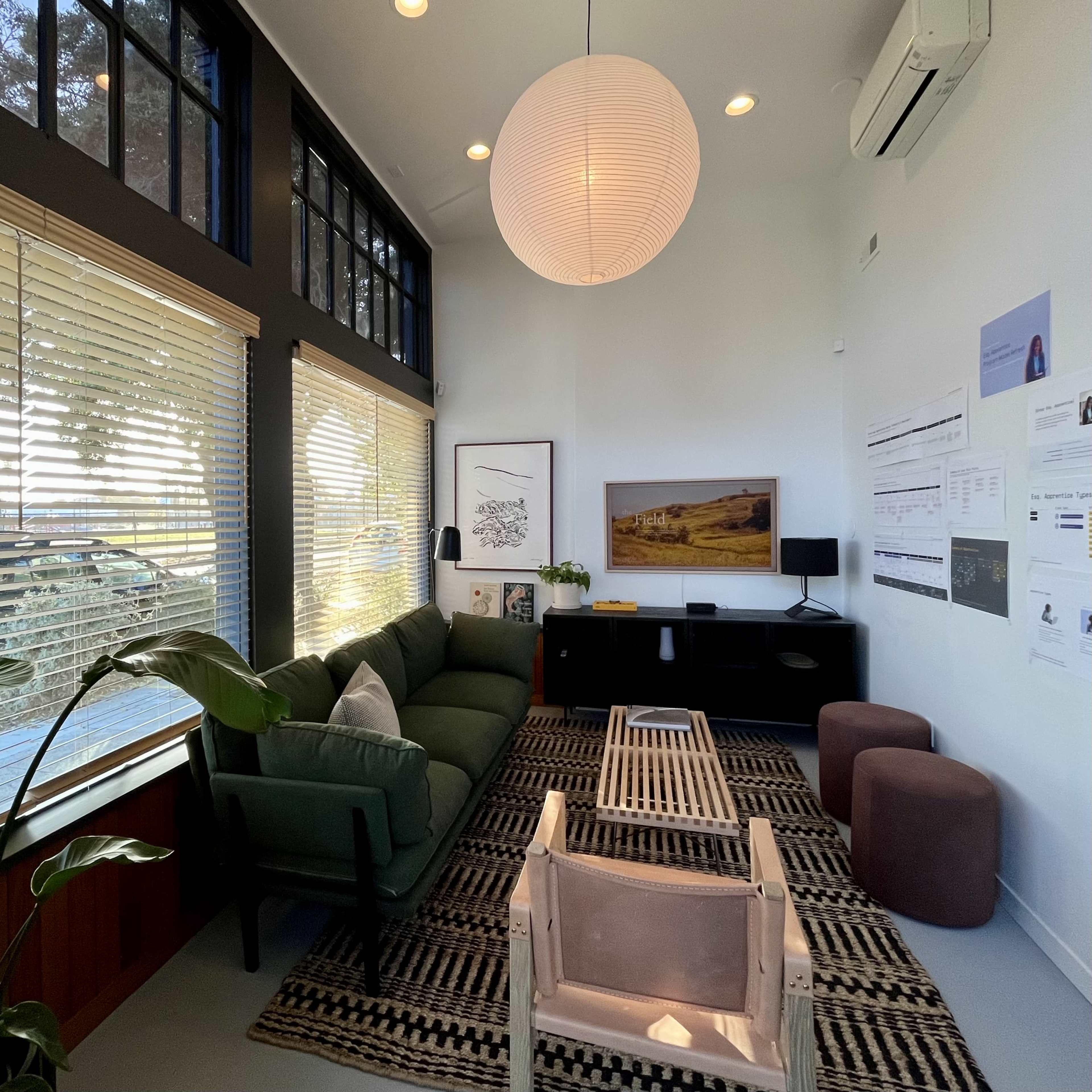 A modern living room with a green sofa, two brown ottomans, a coffee table, and large windows letting in natural light.