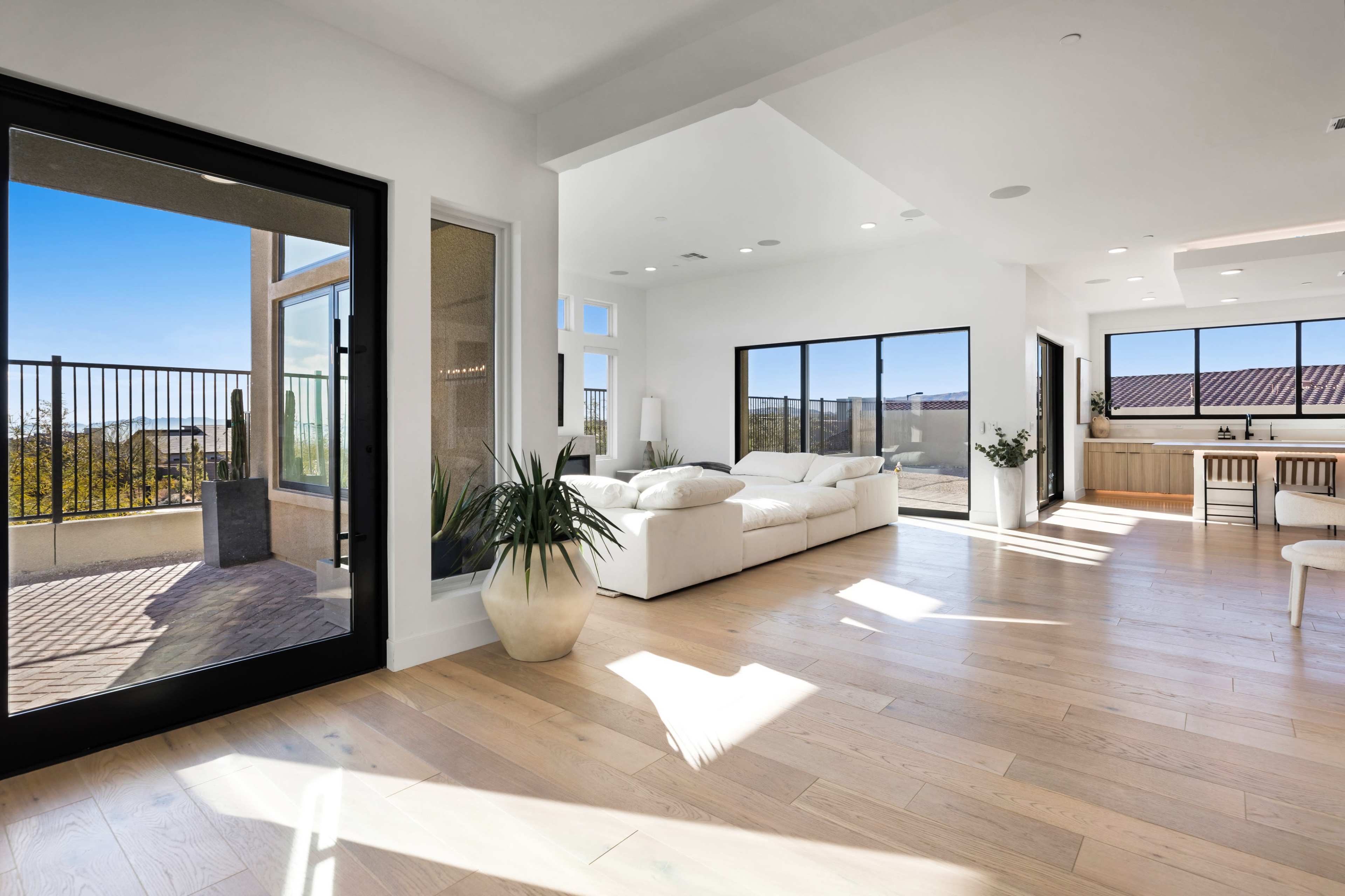 A bright, modern living room with large windows and a white sectional sofa, leading to a balcony with a view.